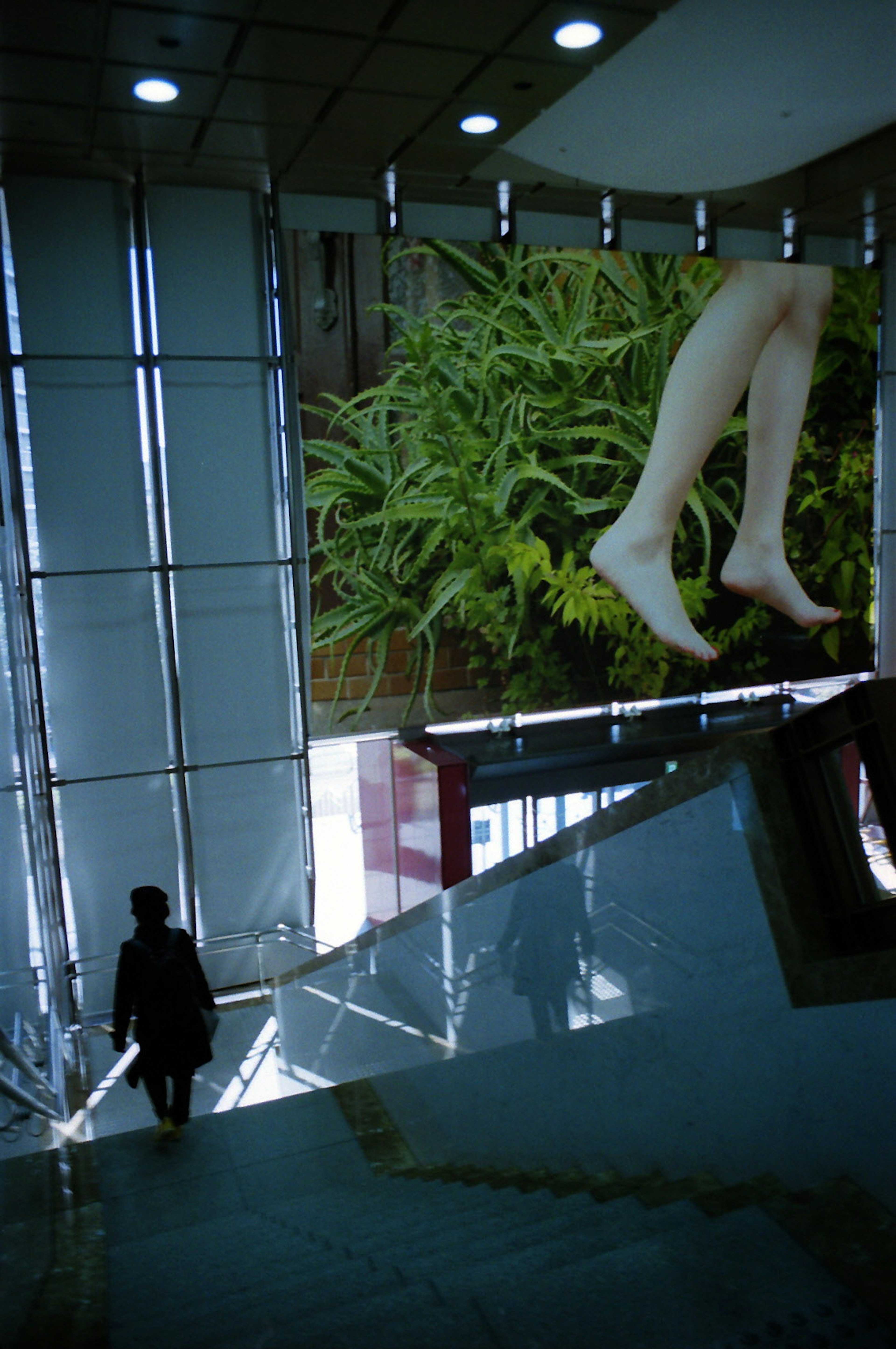 Silhouette of a person in a modern building with a large advertisement of legs against a green background