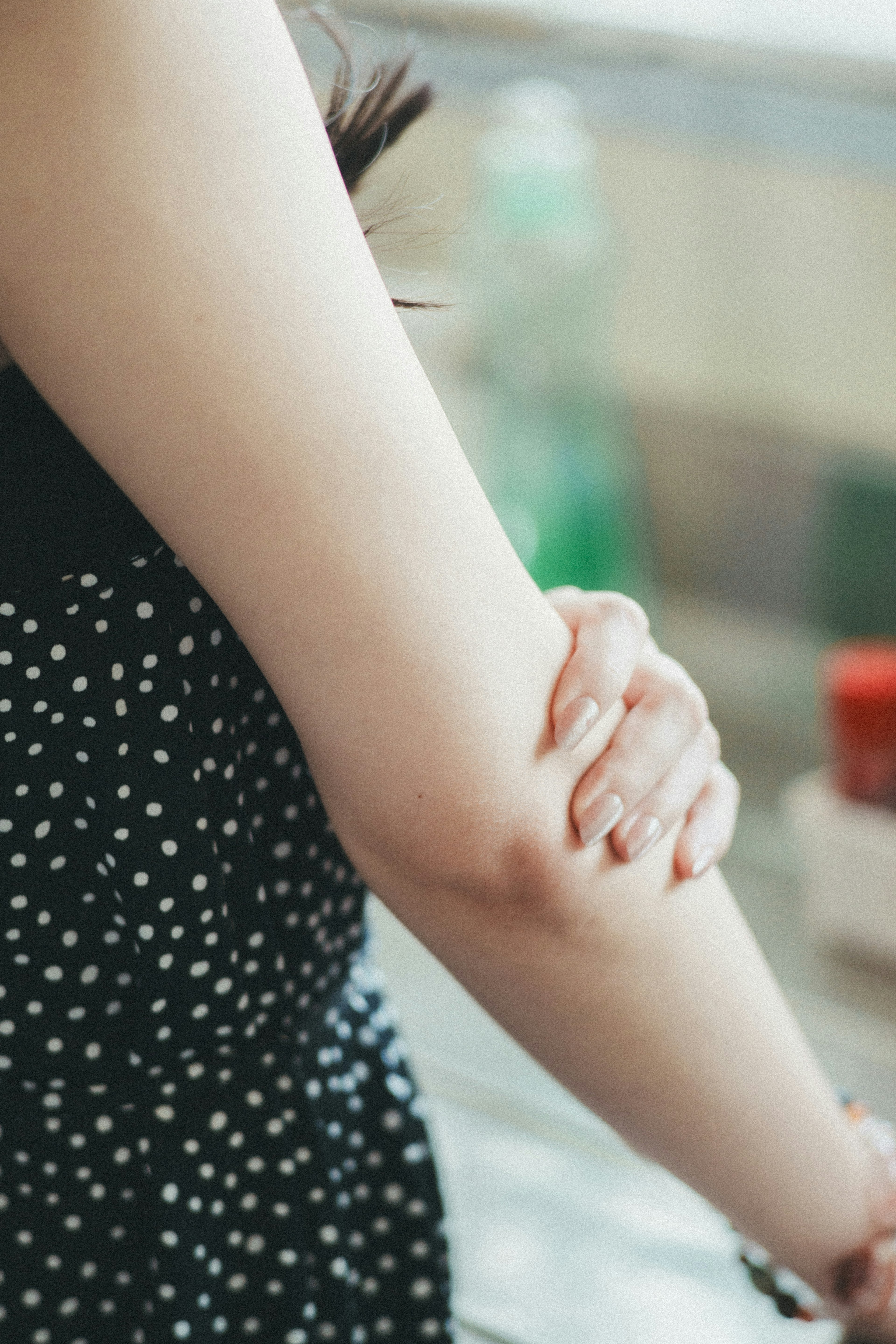 Primer plano del brazo de una mujer con un vestido negro con lunares en un entorno interior