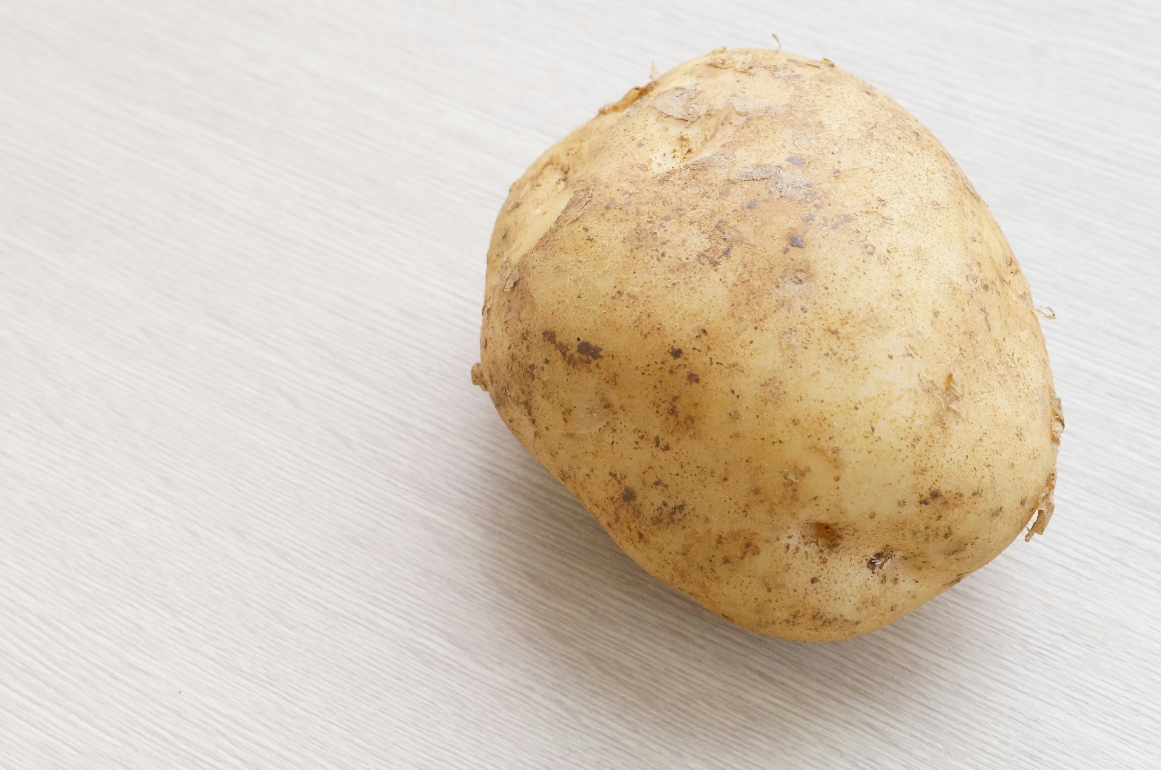 Una papa con tierra colocada sobre una superficie de tela blanca