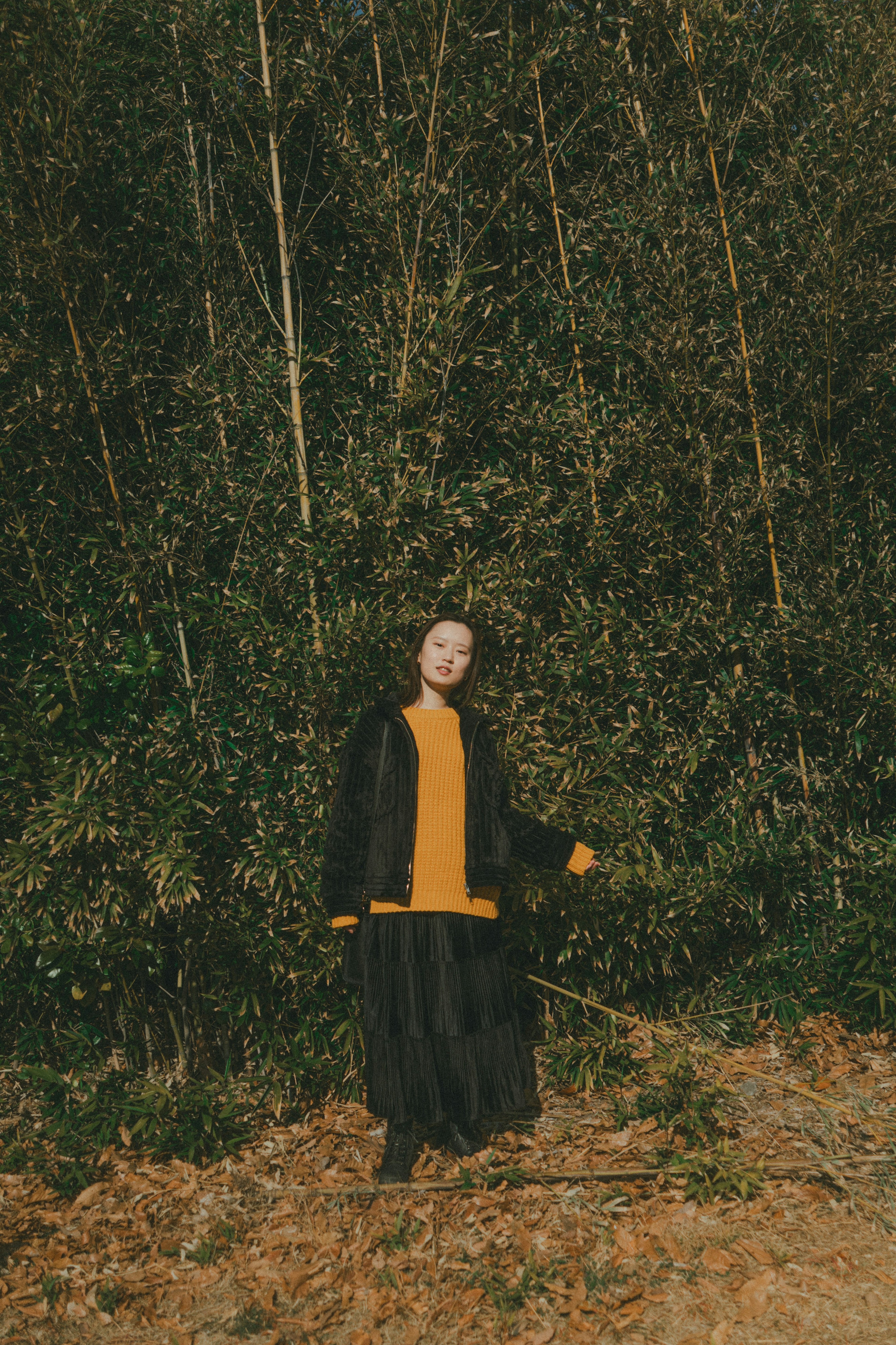 Donna con maglione giallo e gonna nera in piedi davanti a uno sfondo verde