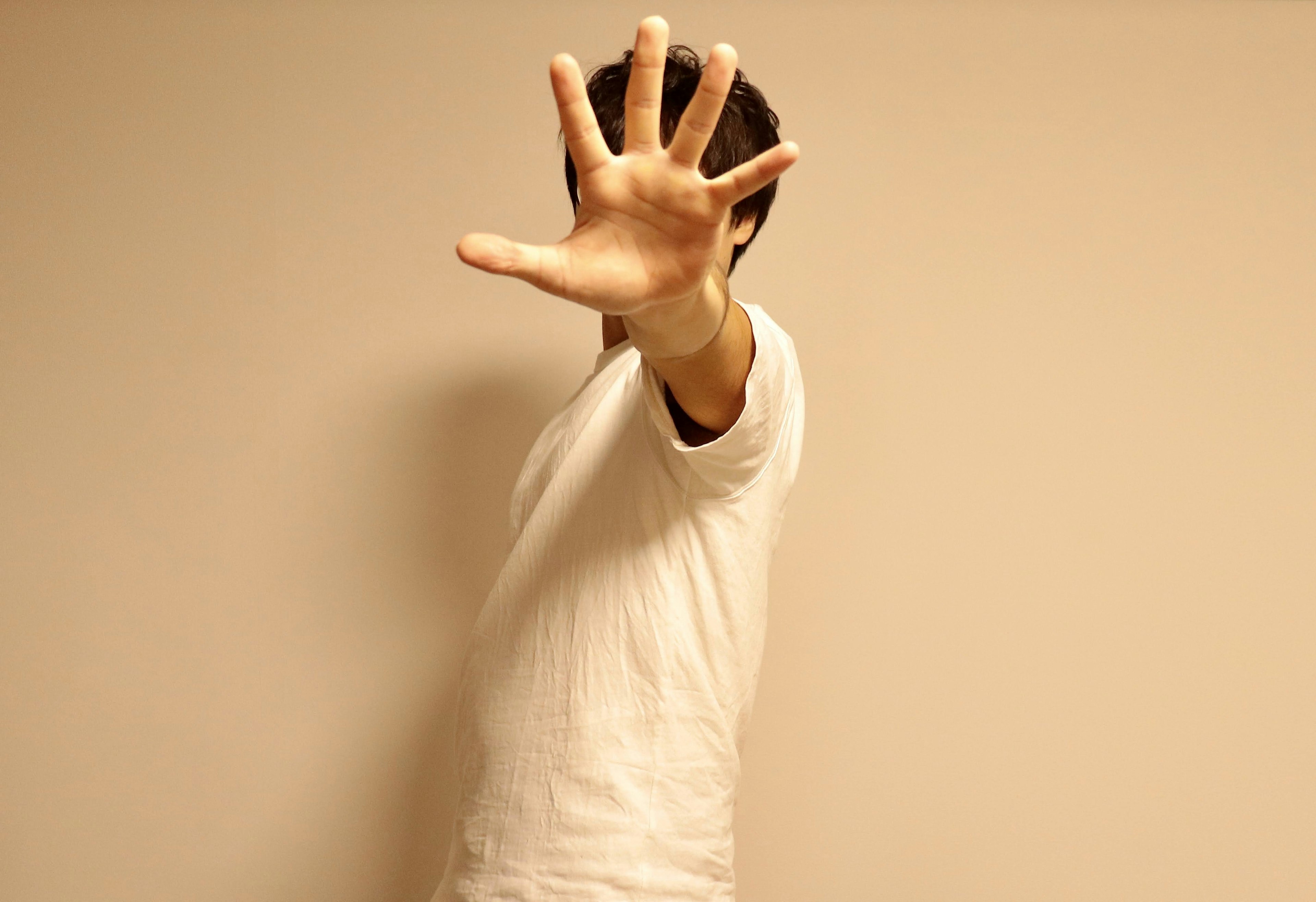 Une personne portant un t-shirt blanc levant la main devant un fond uni