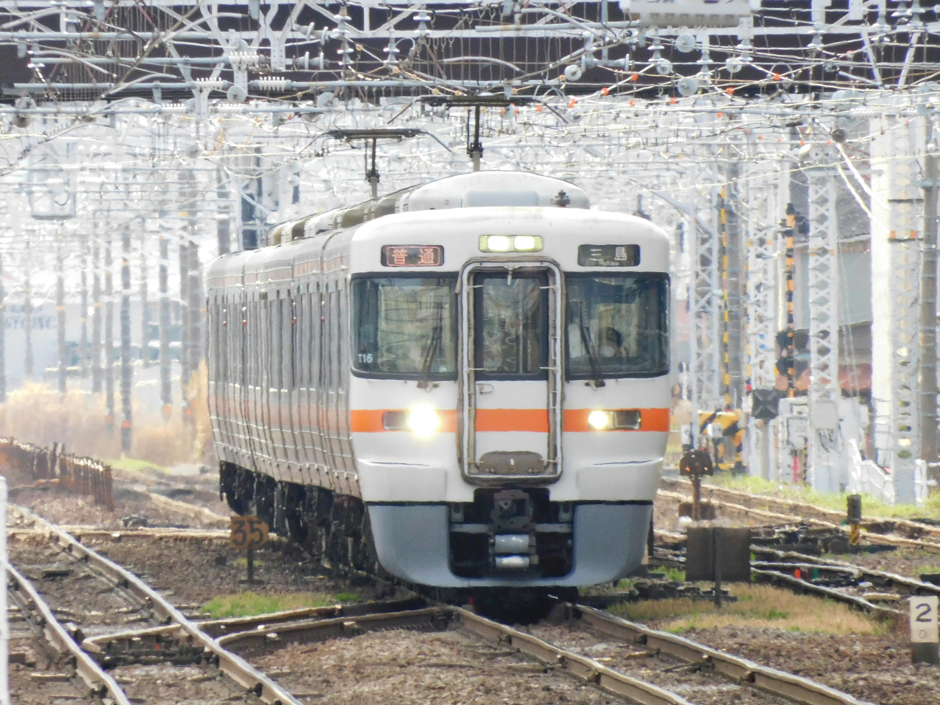 Un vehículo de tren sobre rieles con líneas aéreas e infraestructura ferroviaria al fondo