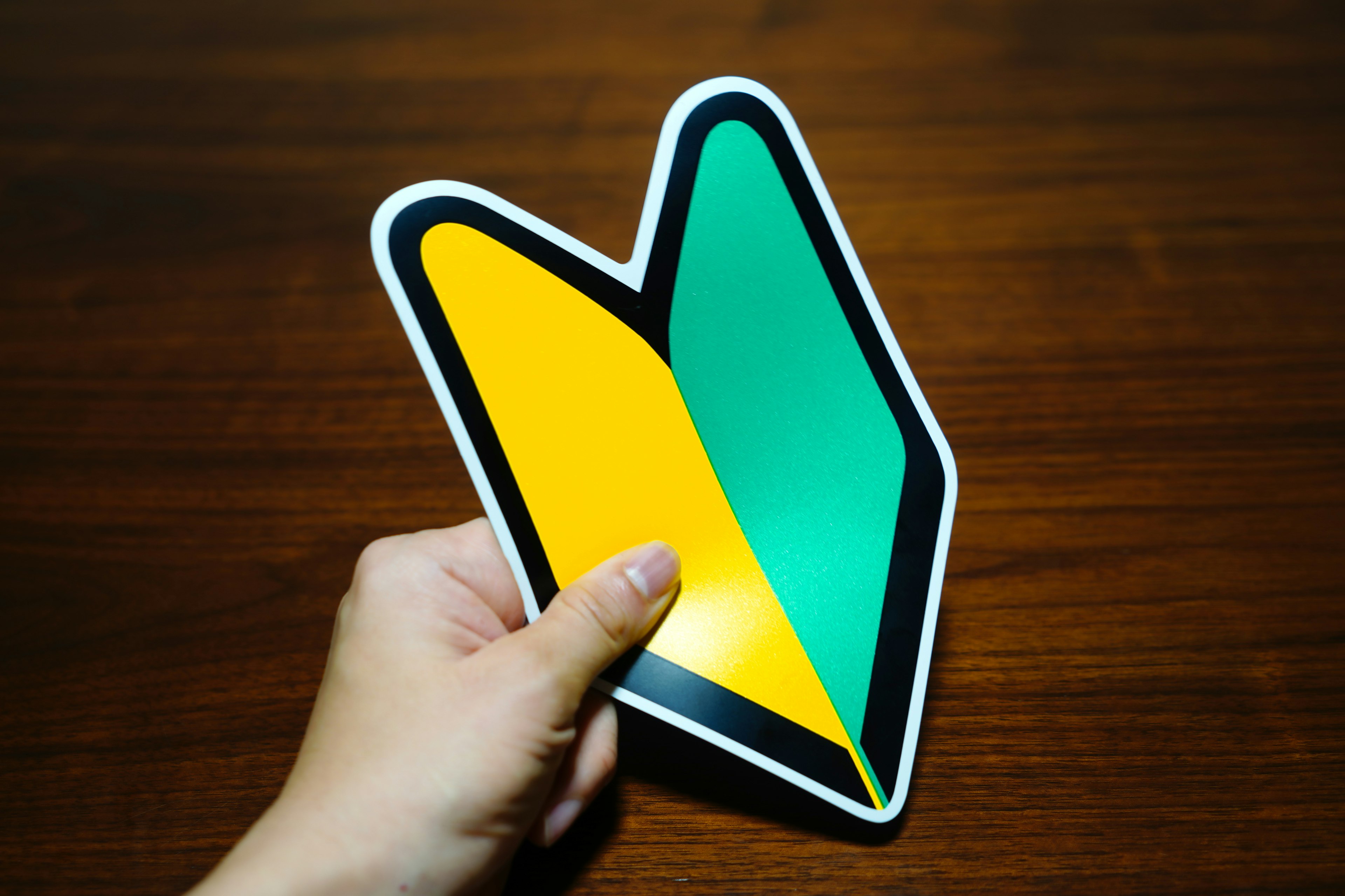 A hand holding a yellow and green symbol sticker