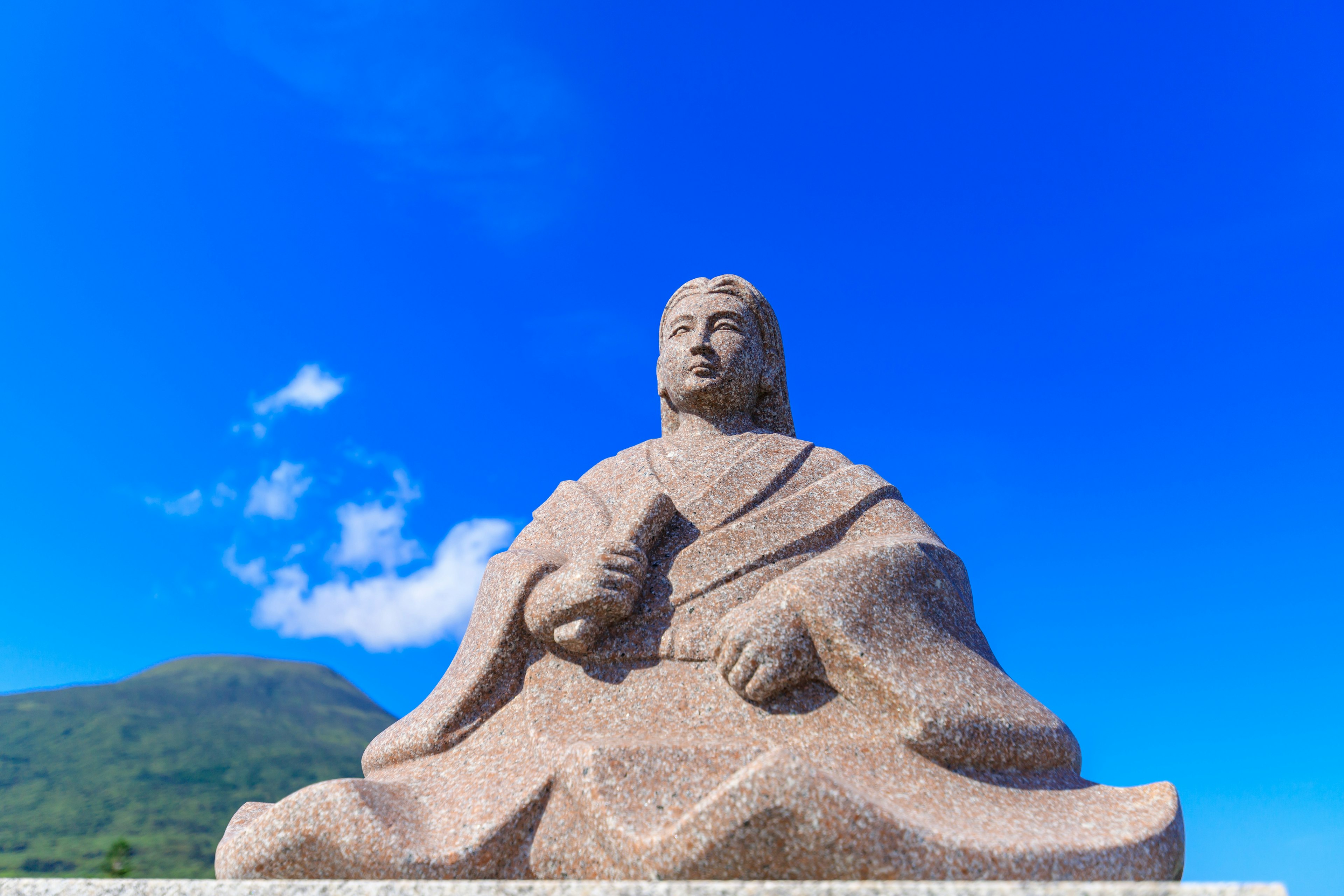 A seated stone statue of a figure against a blue sky