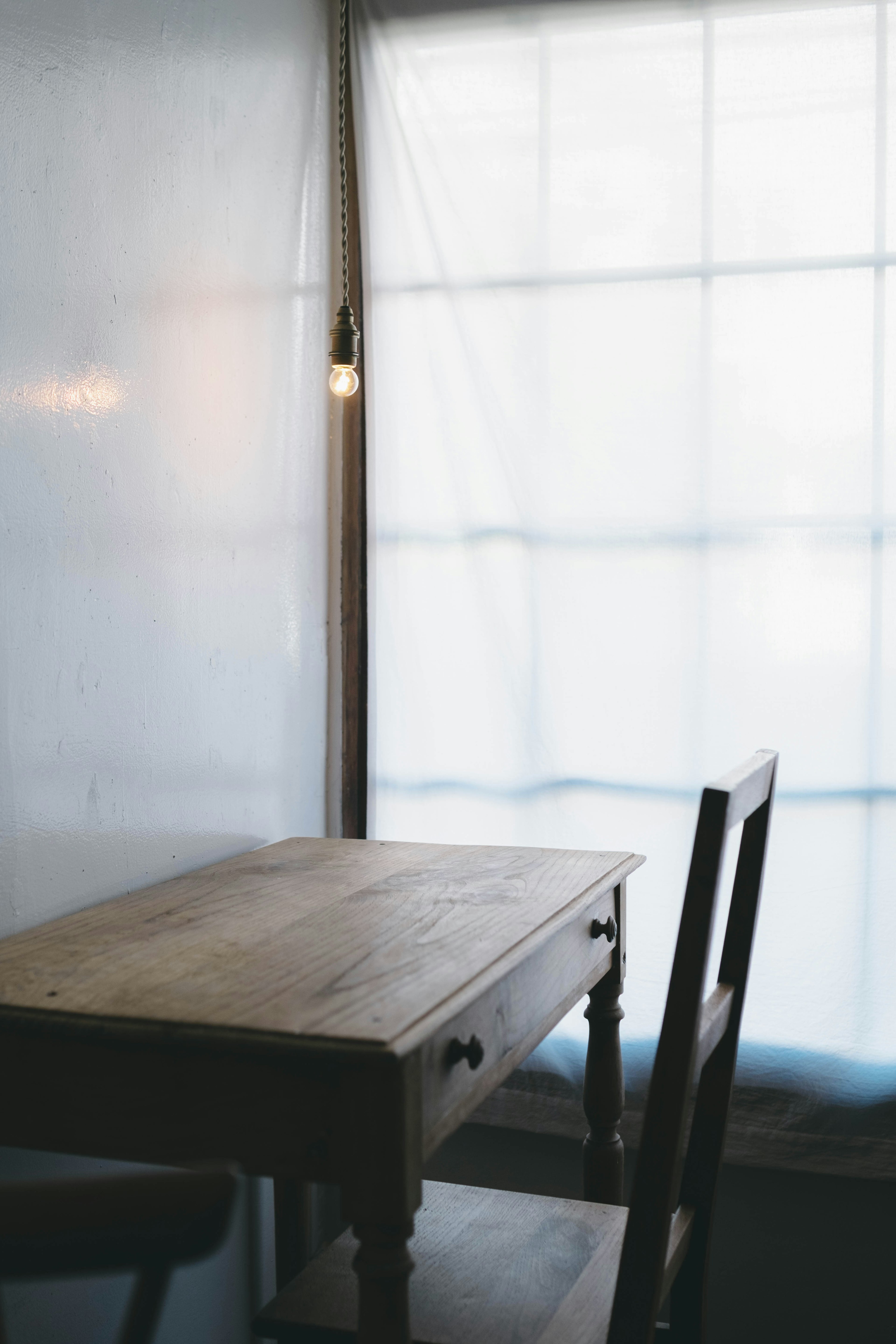 Interior simple con una mesa de madera y una silla cerca de una ventana brillante