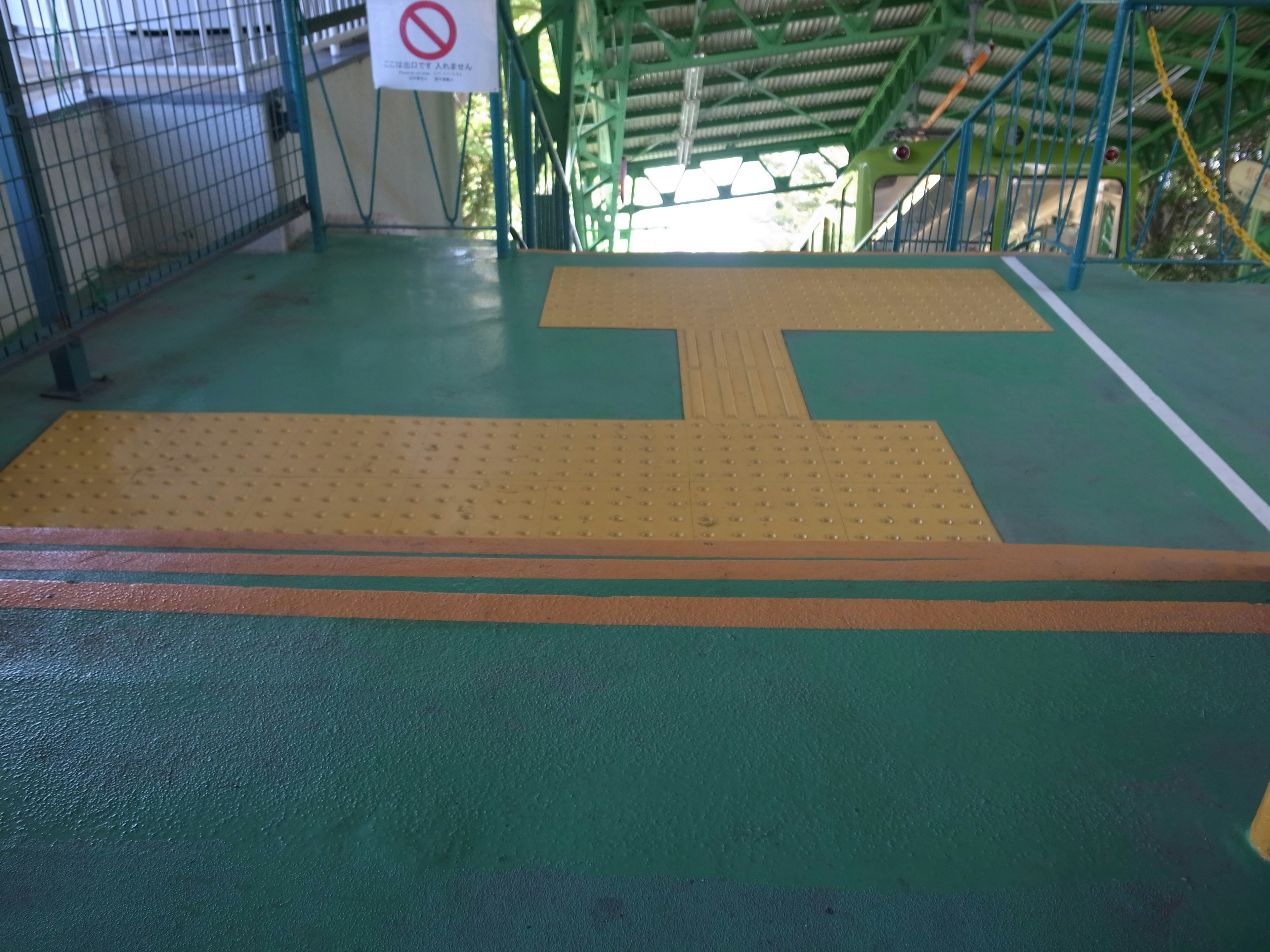 Sol vert avec des lignes orange et un revêtement tactile près d'un escalier