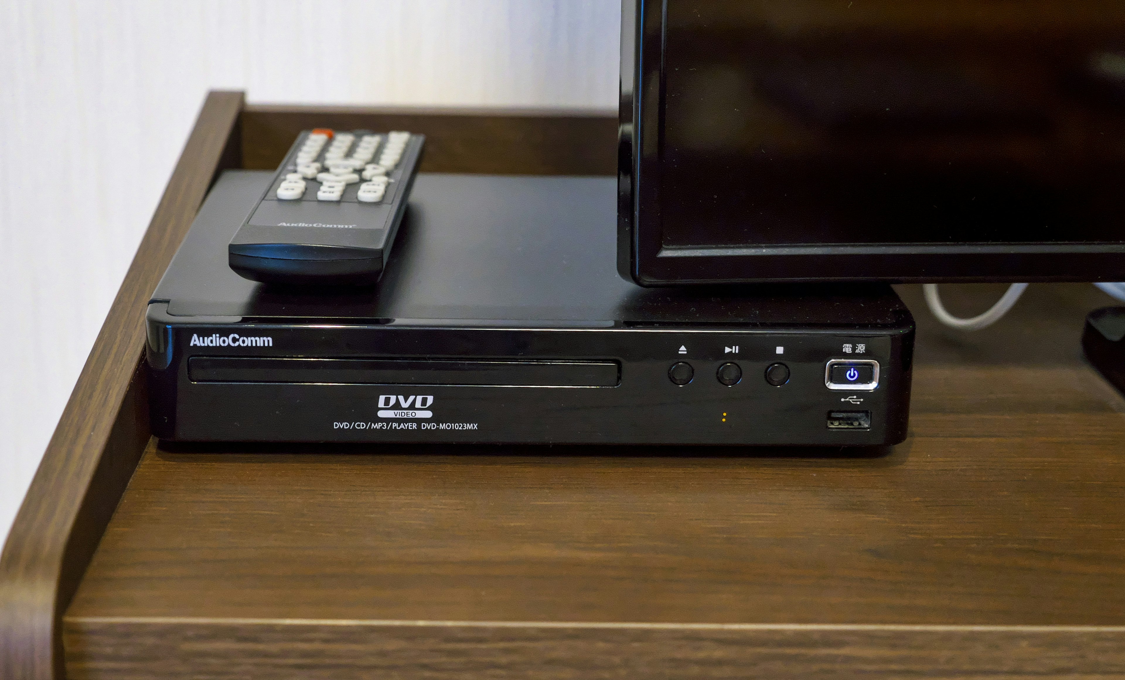 Black DVD player placed on a wooden table alongside a remote and a television