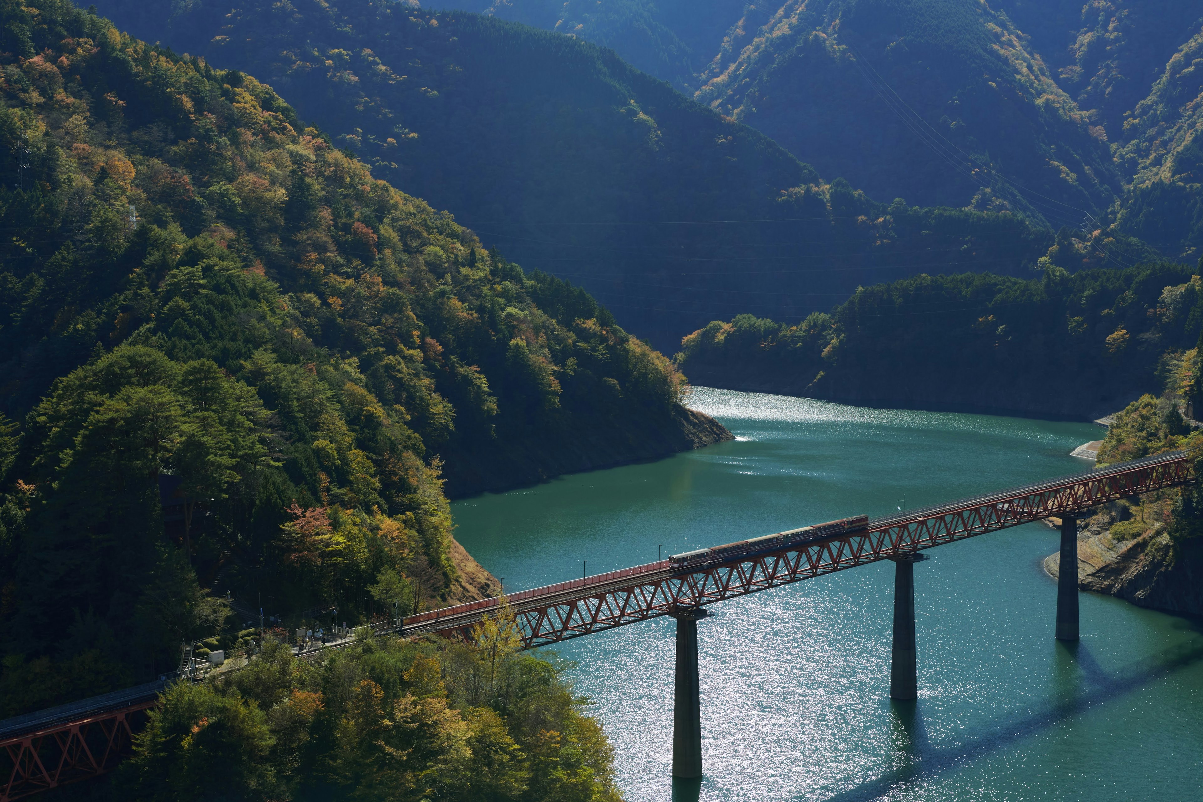 Railway bridge over a green lake surrounded by mountains