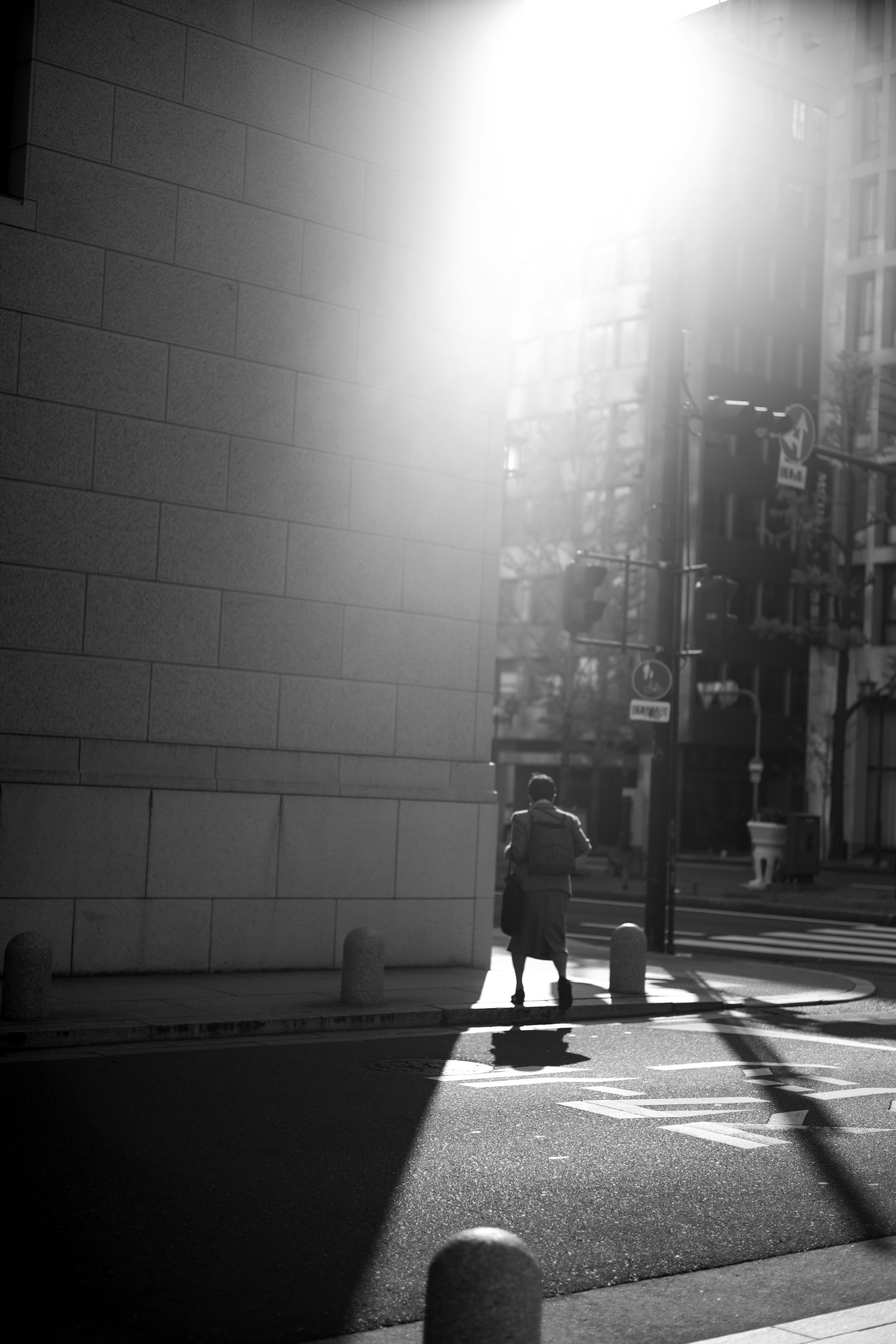 Black and white street corner scene with light streaming in a person standing near a wall