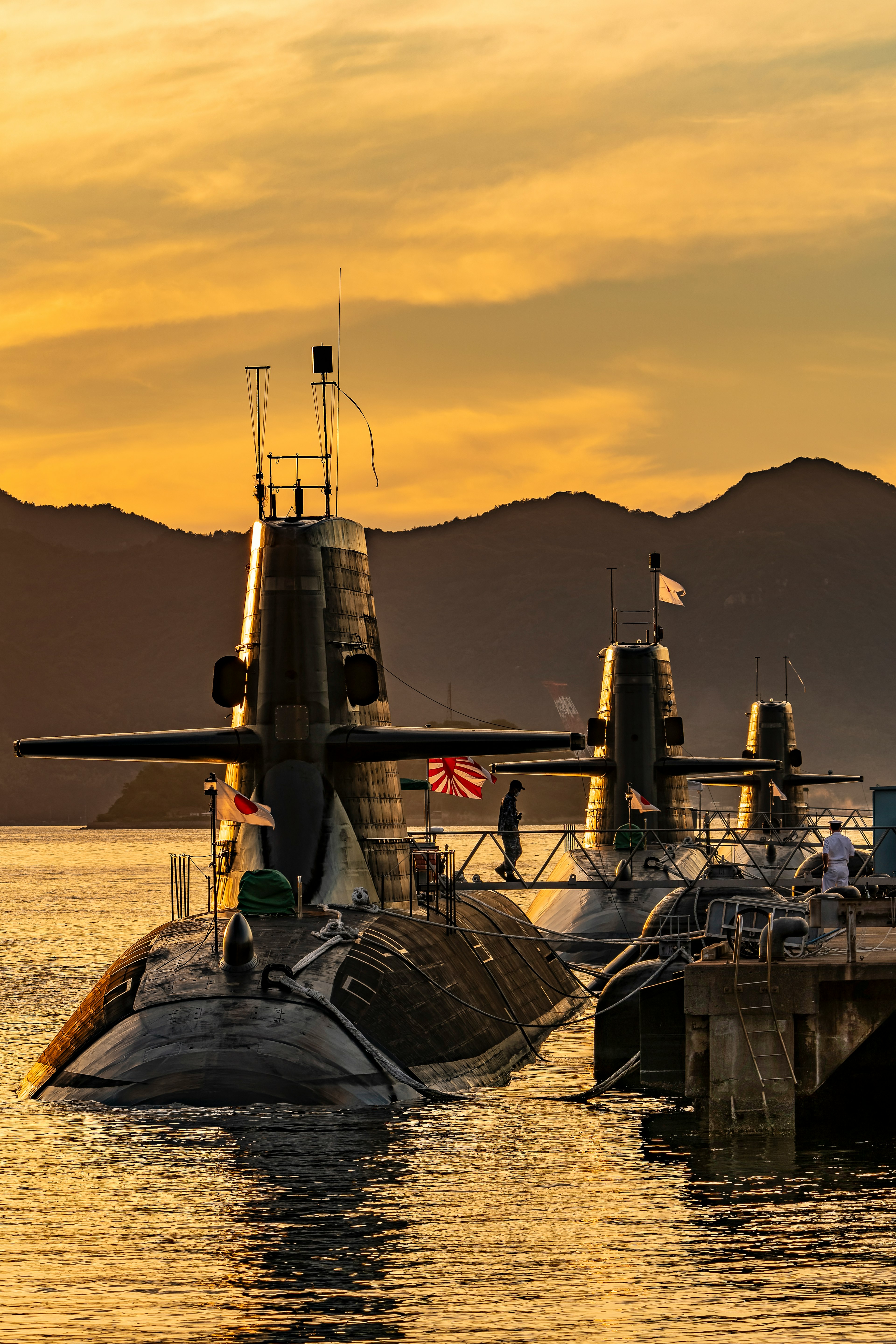 Submarines docked at sunset with mountains in the background