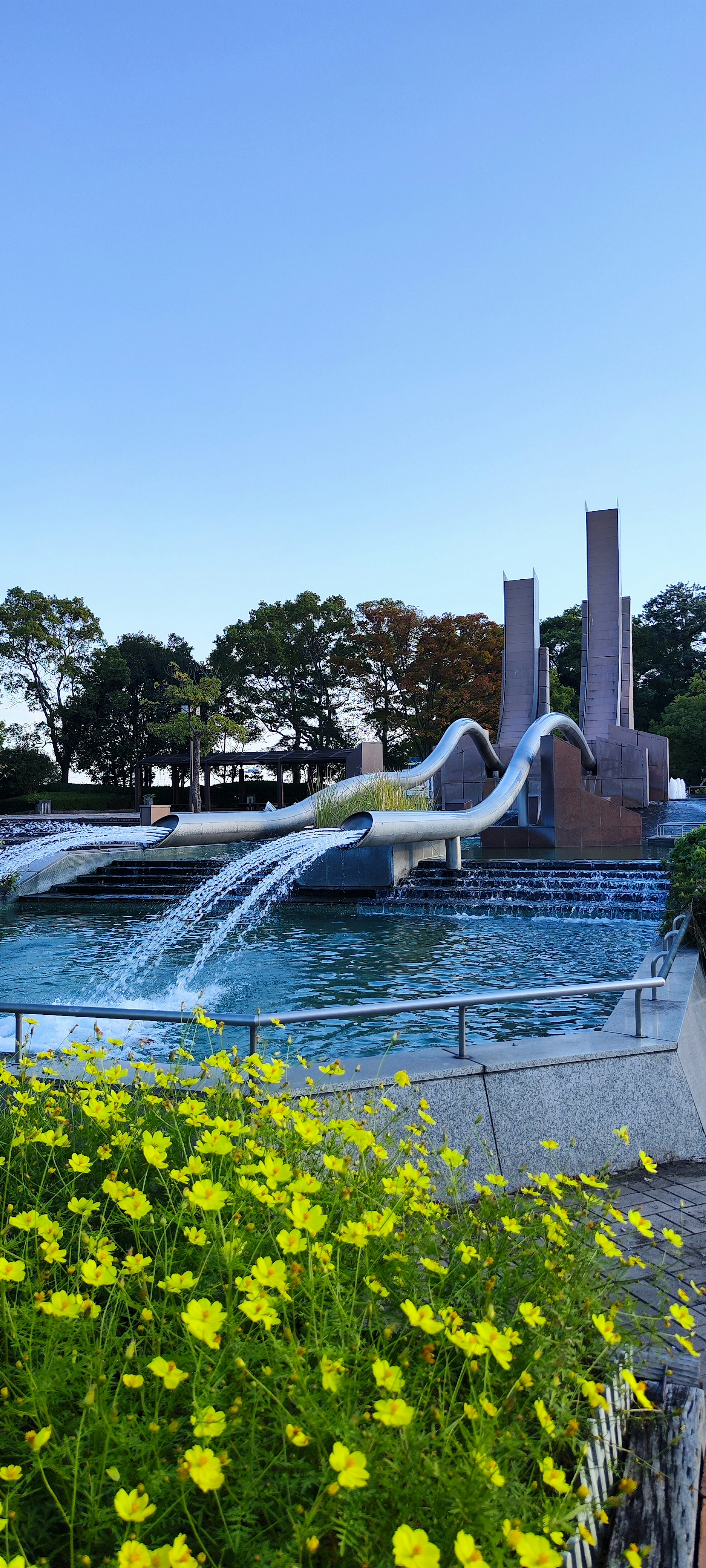 Landscape featuring a fountain and yellow flowers under a blue sky