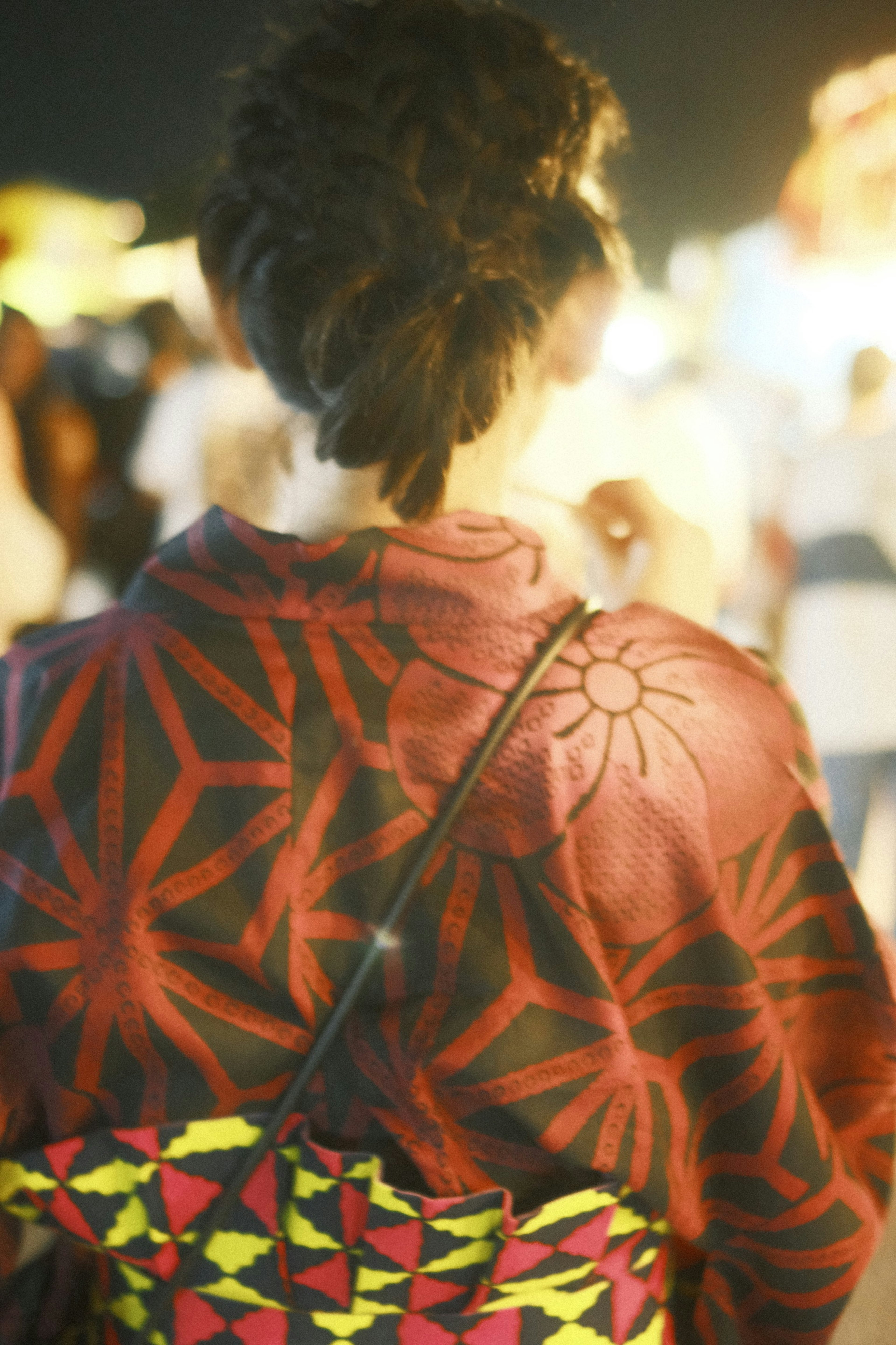 Woman wearing a red patterned kimono with a floral design seen from the back with people in the background