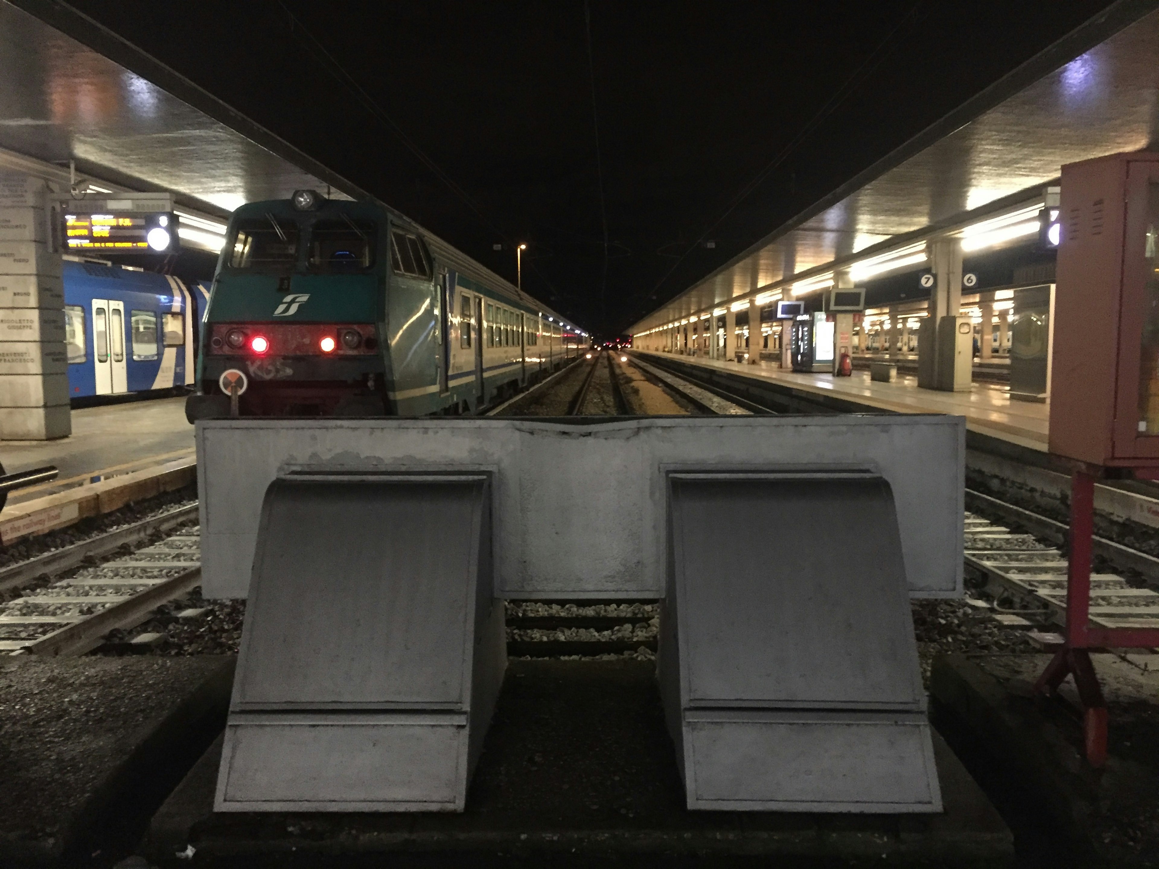 Nighttime view of a train station with a train at the platform and structures on either side of the tracks