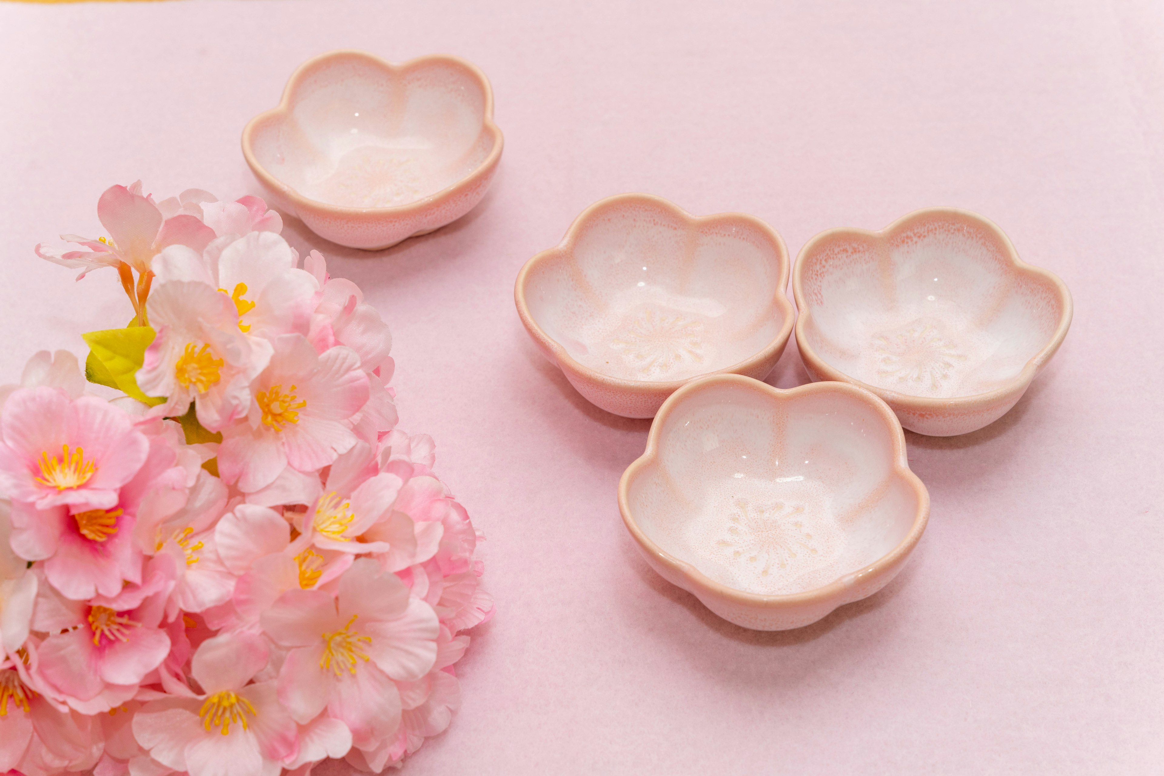 Four pink flower-shaped bowls arranged with a bouquet of cherry blossoms nearby