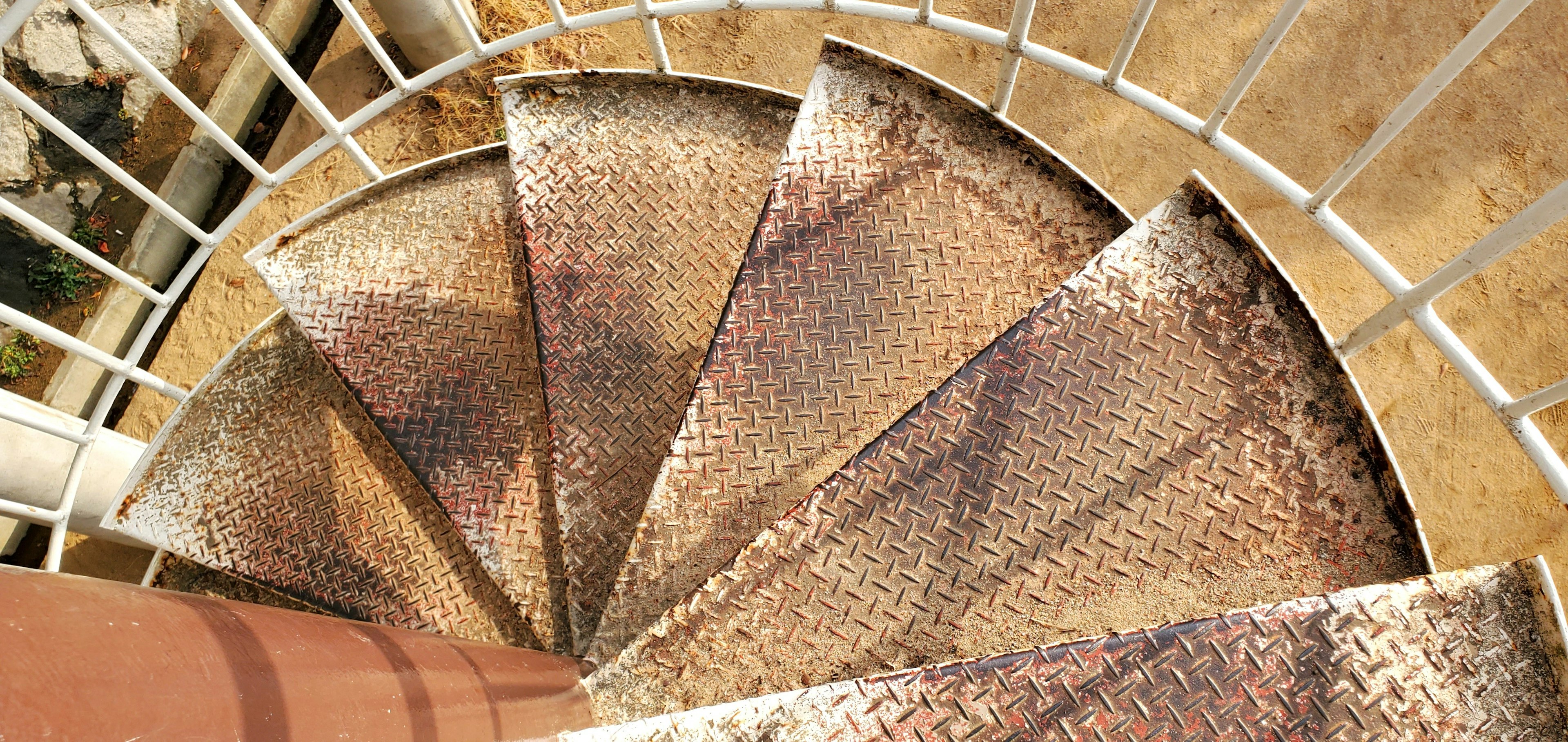 Image of a spiral staircase viewed from above showing rusty metal steps and a metal railing