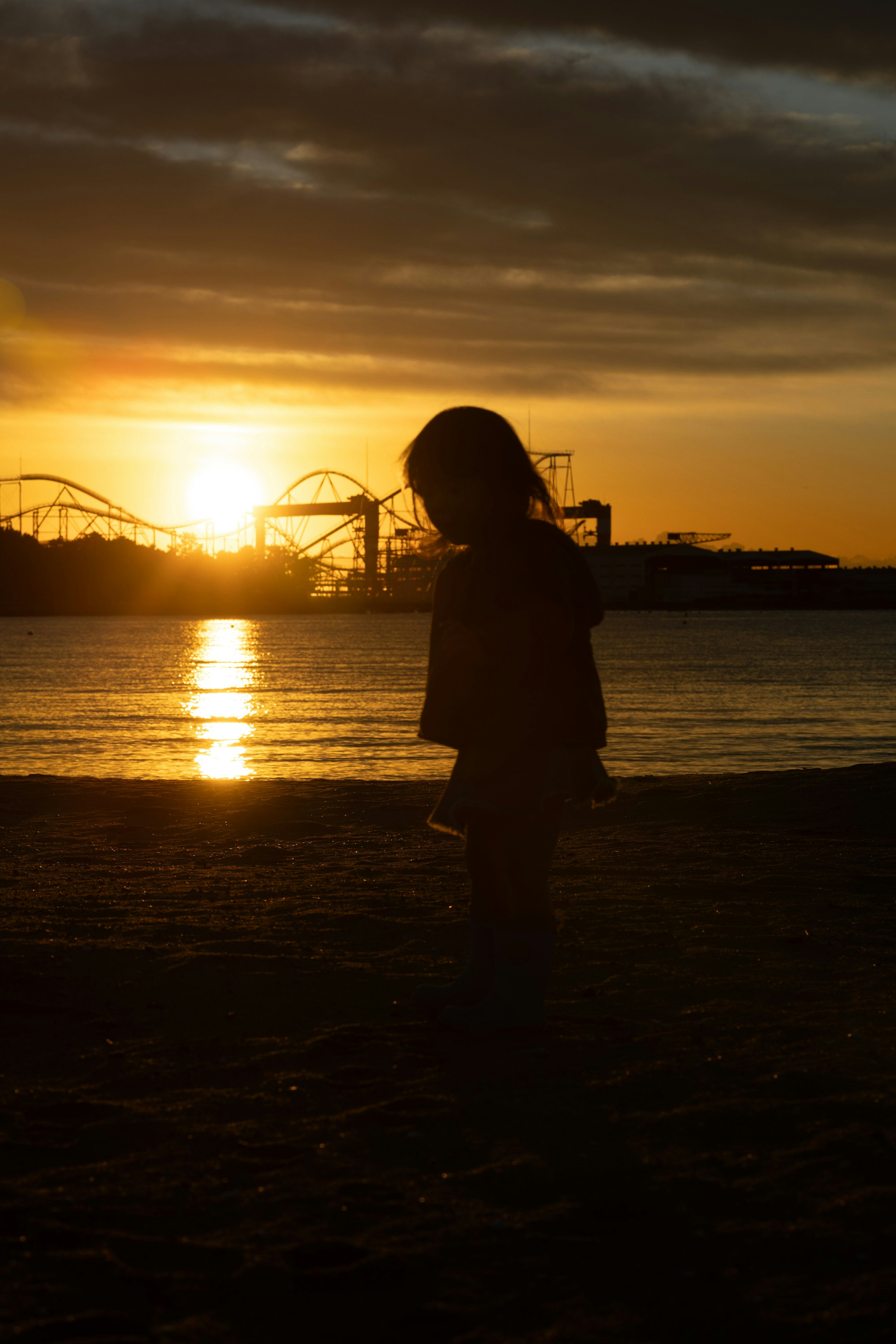 Silhouette d'un enfant contre un coucher de soleil Scène de plage avec des attractions de parc d'attractions au loin
