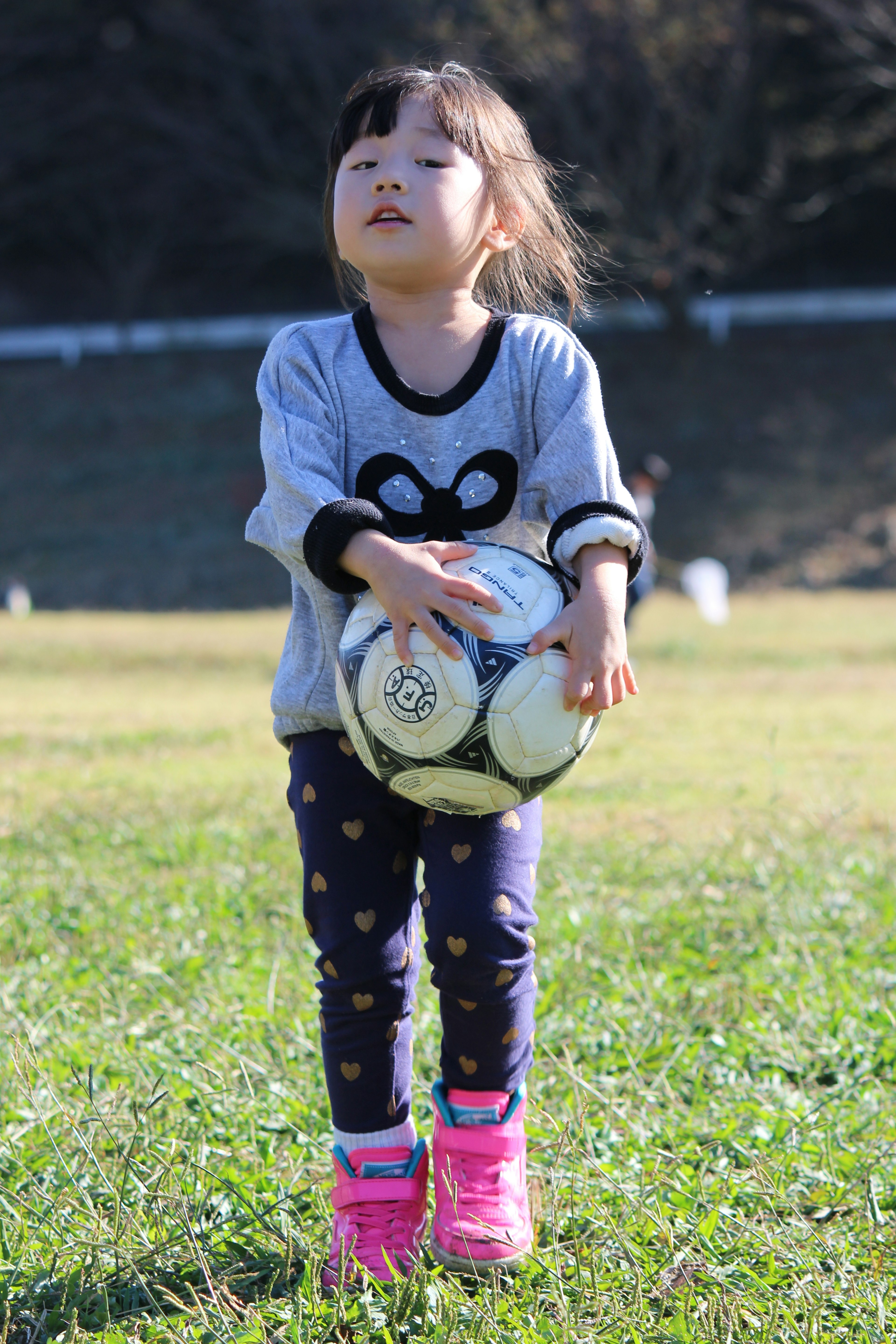 サッカーボールを抱えた小さな女の子が草の上に立っている