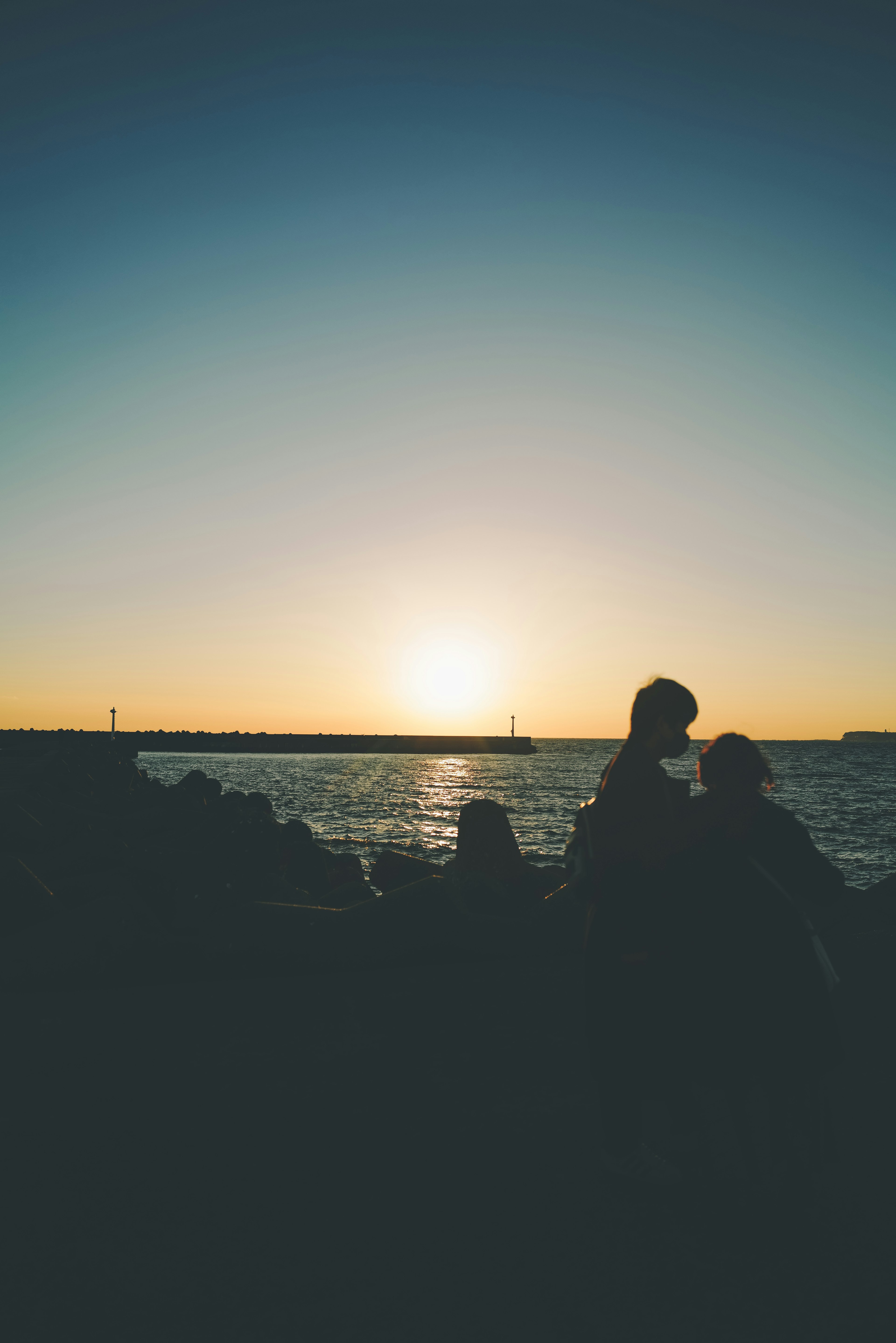 Siluetas de personas junto al mar con el atardecer de fondo