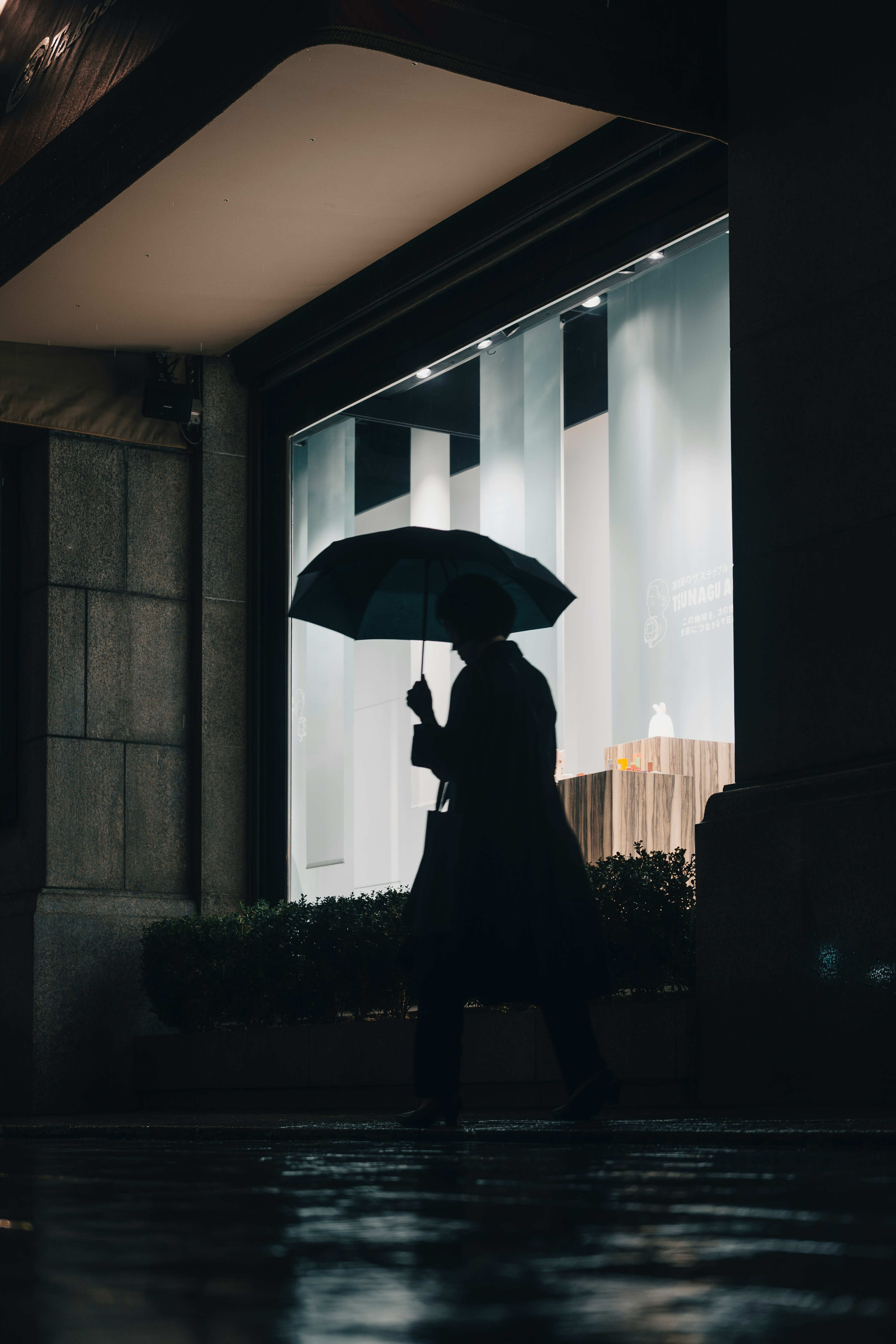 Silhouette of a person walking with an umbrella in a rainy urban setting