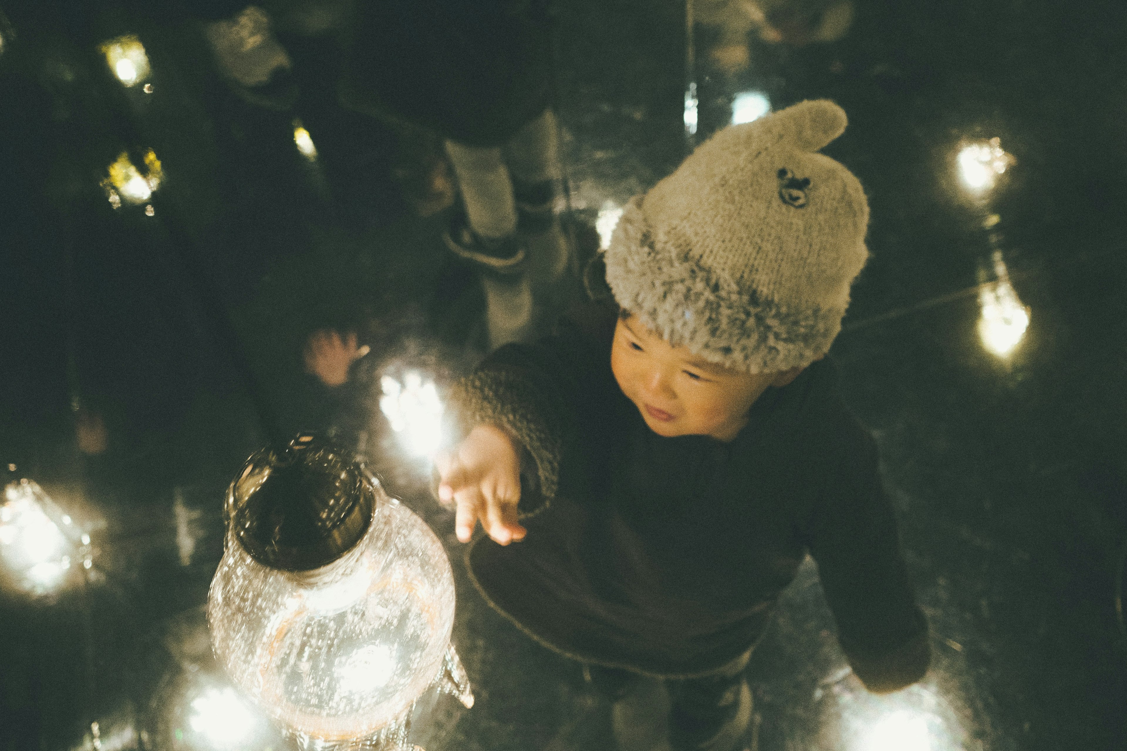 Enfant touchant une lanterne entourée de lumières douces