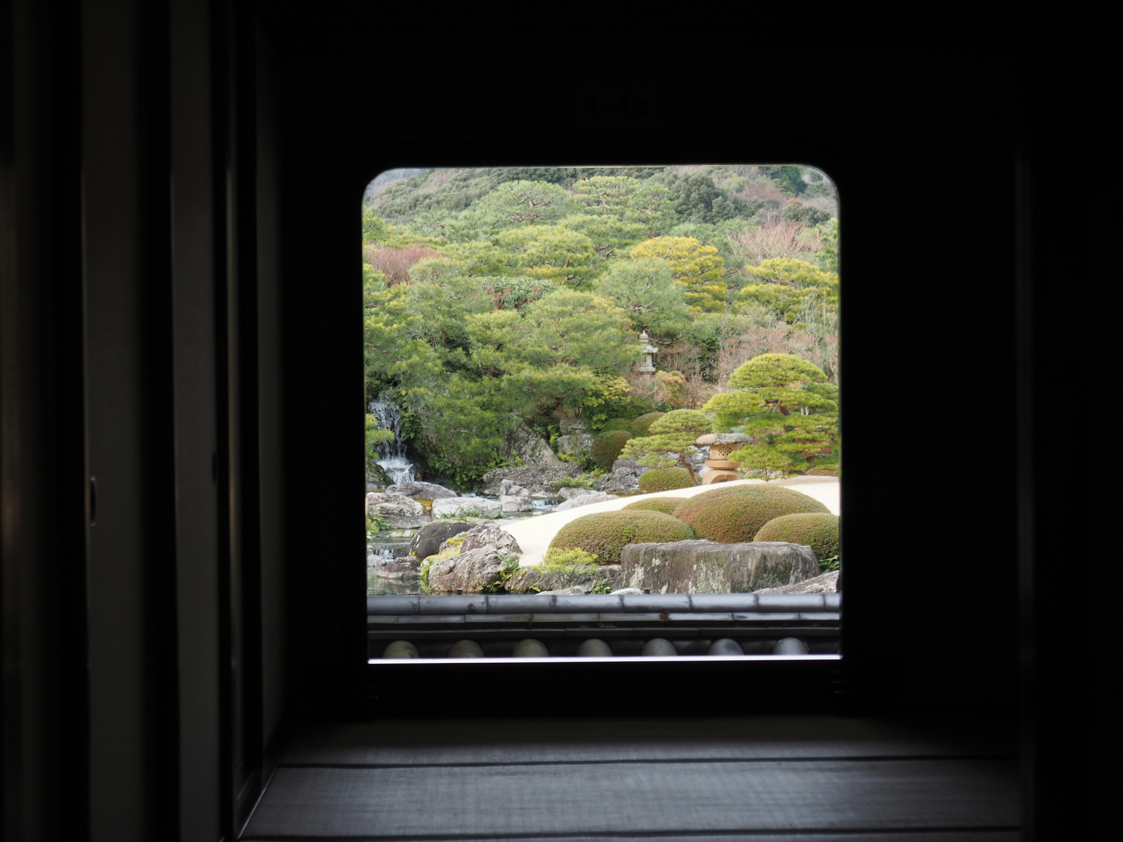 View of a beautiful Japanese garden through a window featuring green trees and stone arrangements