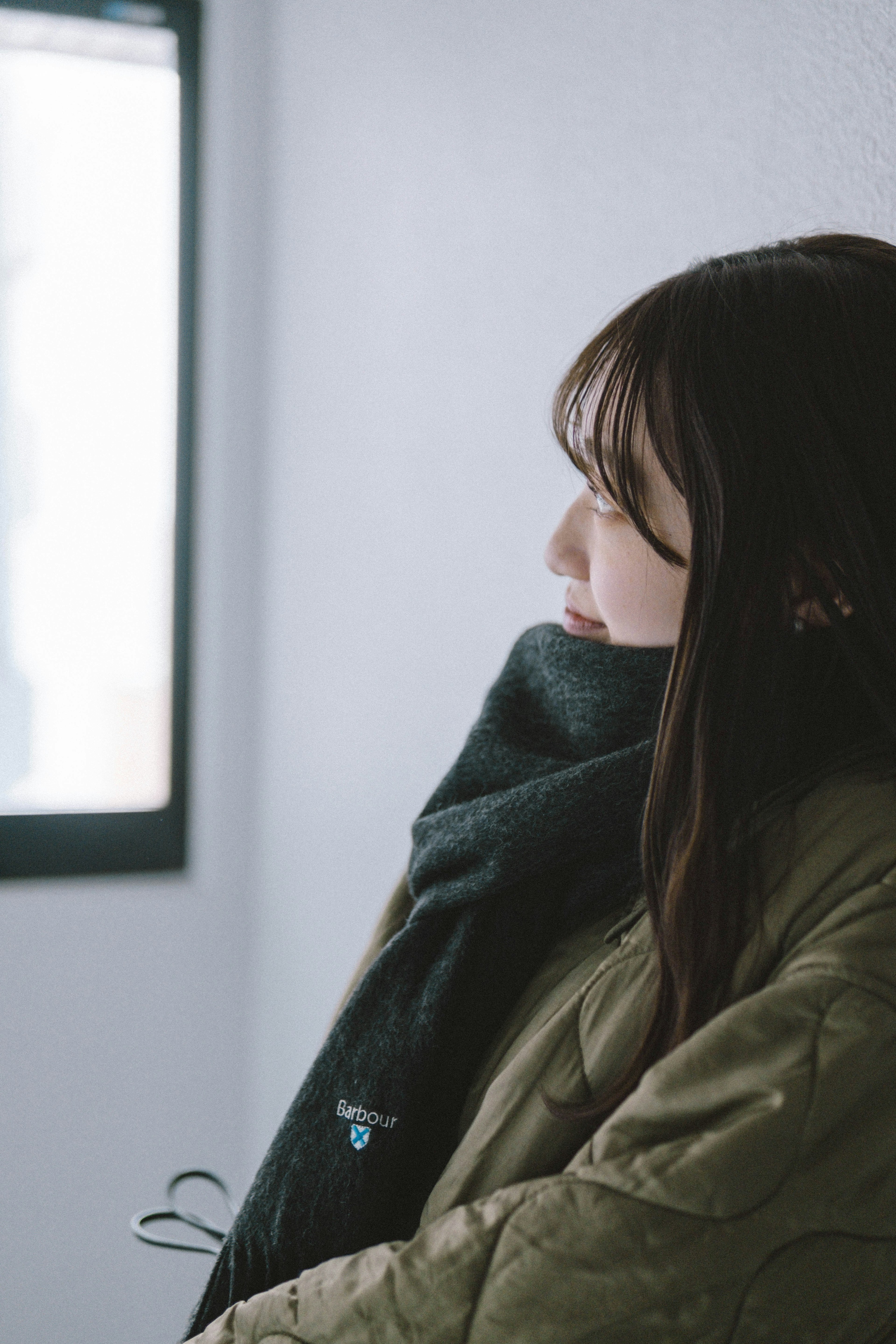 Eine Frau, die seitlich am Fenster steht und einen warmen Mantel und einen Schal trägt