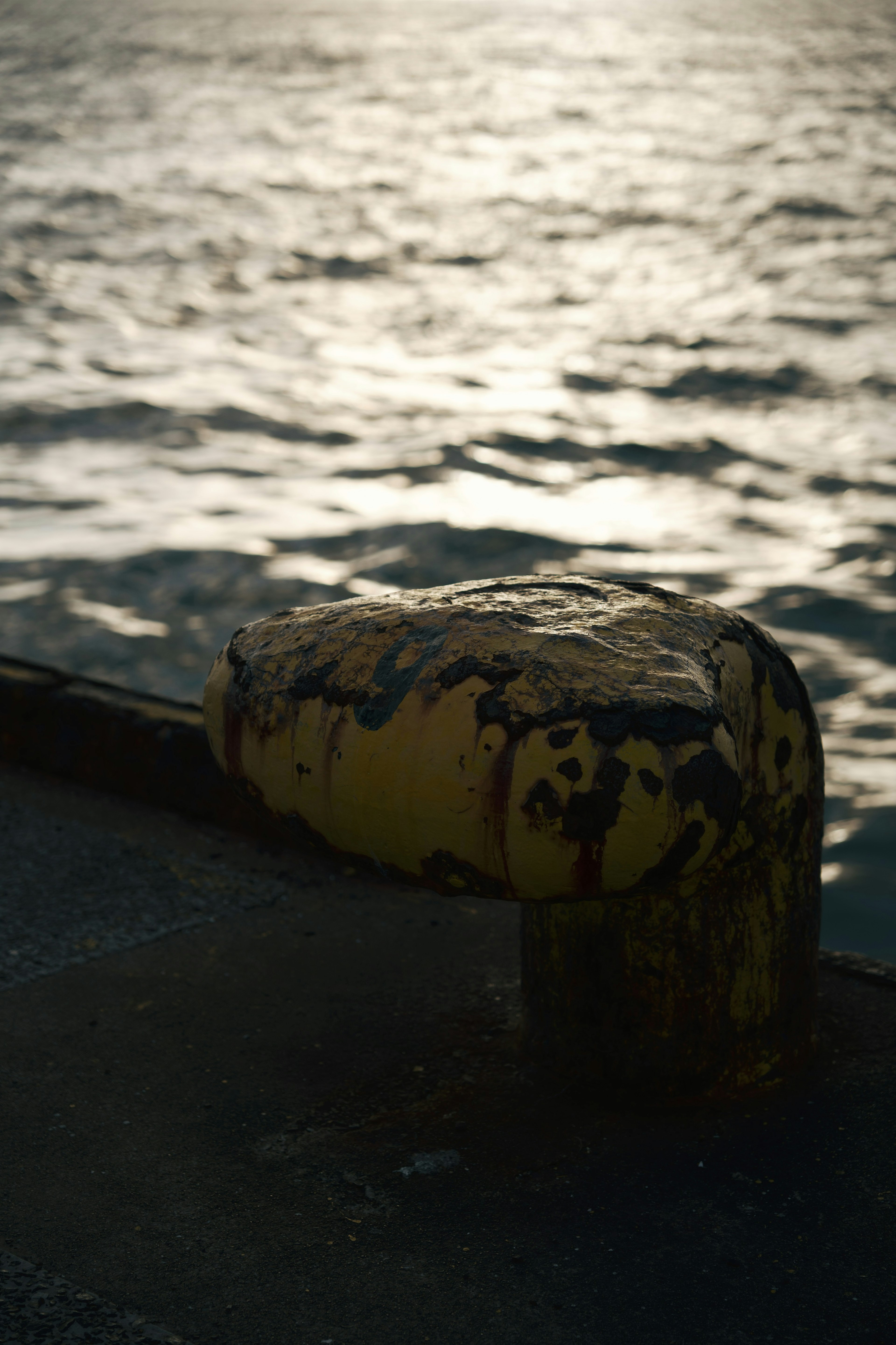 Alter gelber Mooring-Pfosten mit verschwommenem Wasserhintergrund