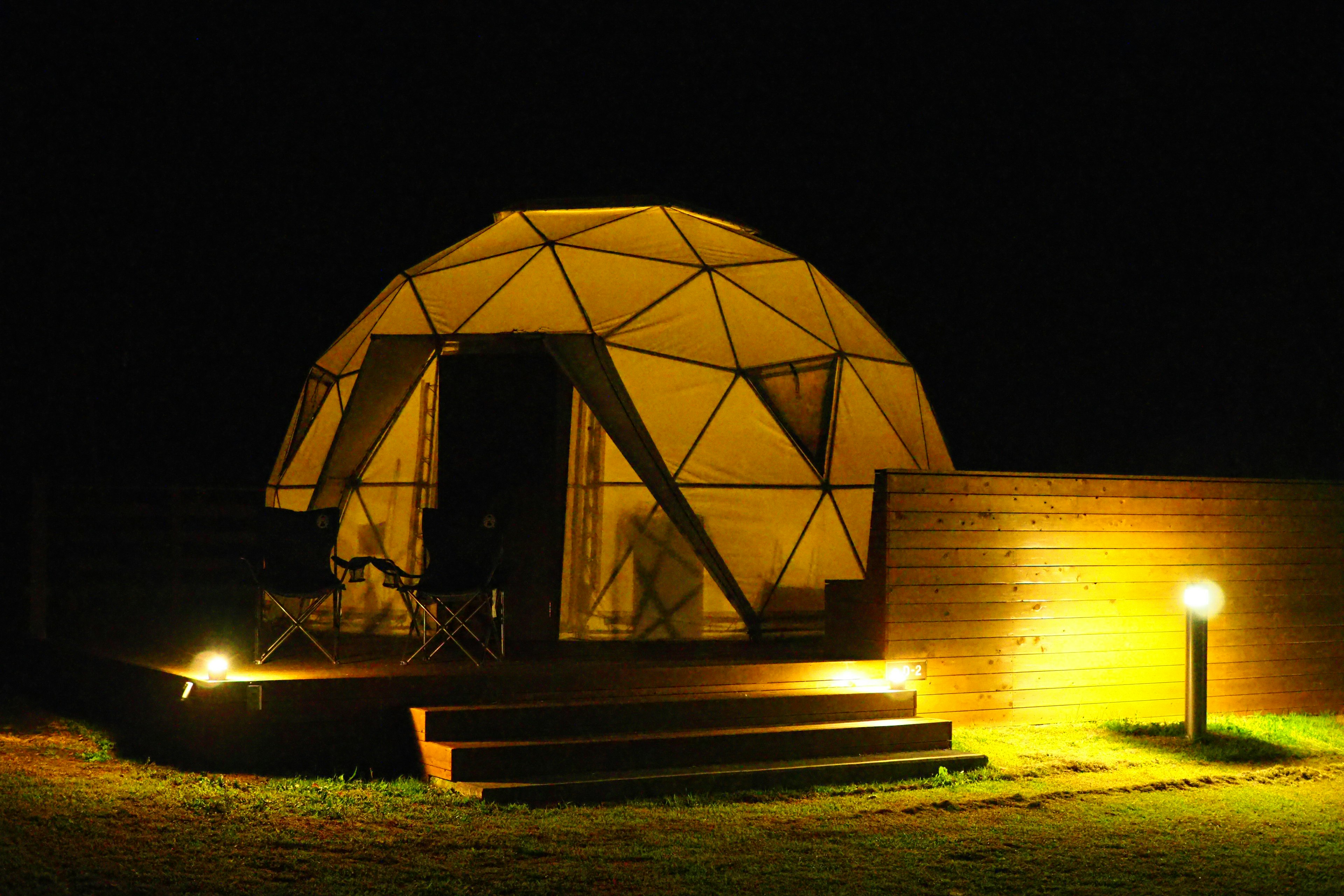 Structure en dôme géodésique éclairée la nuit avec une terrasse en bois