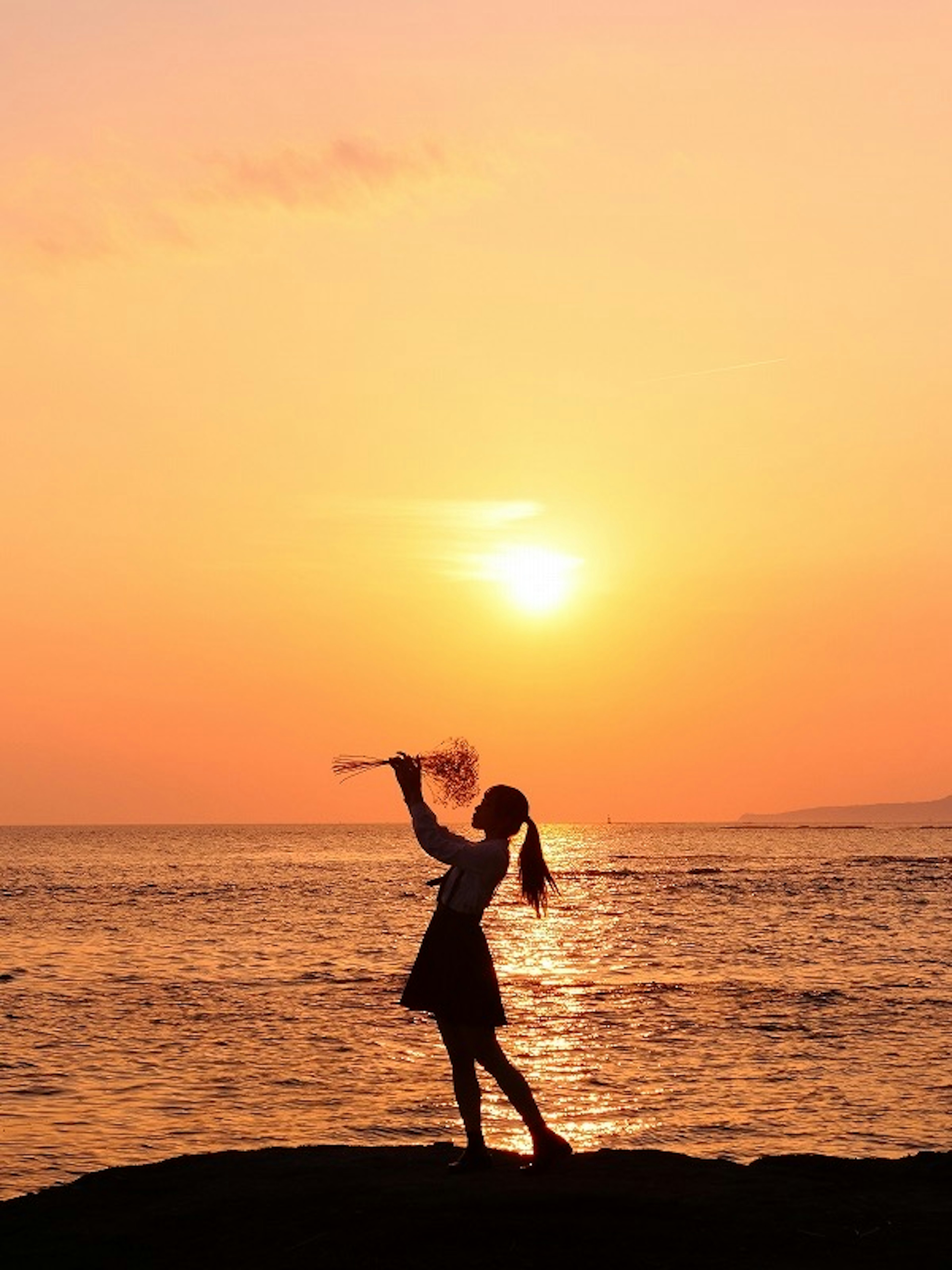 Silhouette eines Mädchens, das am Meer mit Sonnenuntergang im Hintergrund tanzt