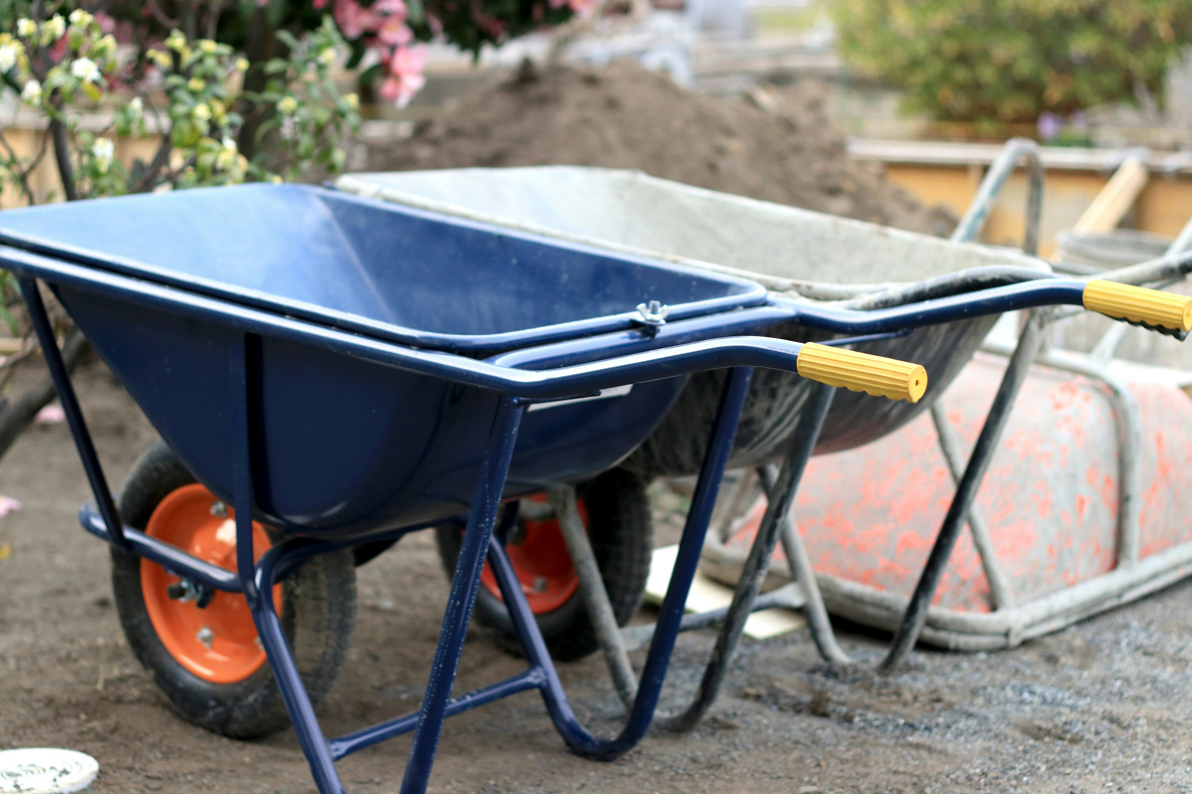 Eine blaue Schubkarre und eine graue Schubkarre nebeneinander in einem Garten