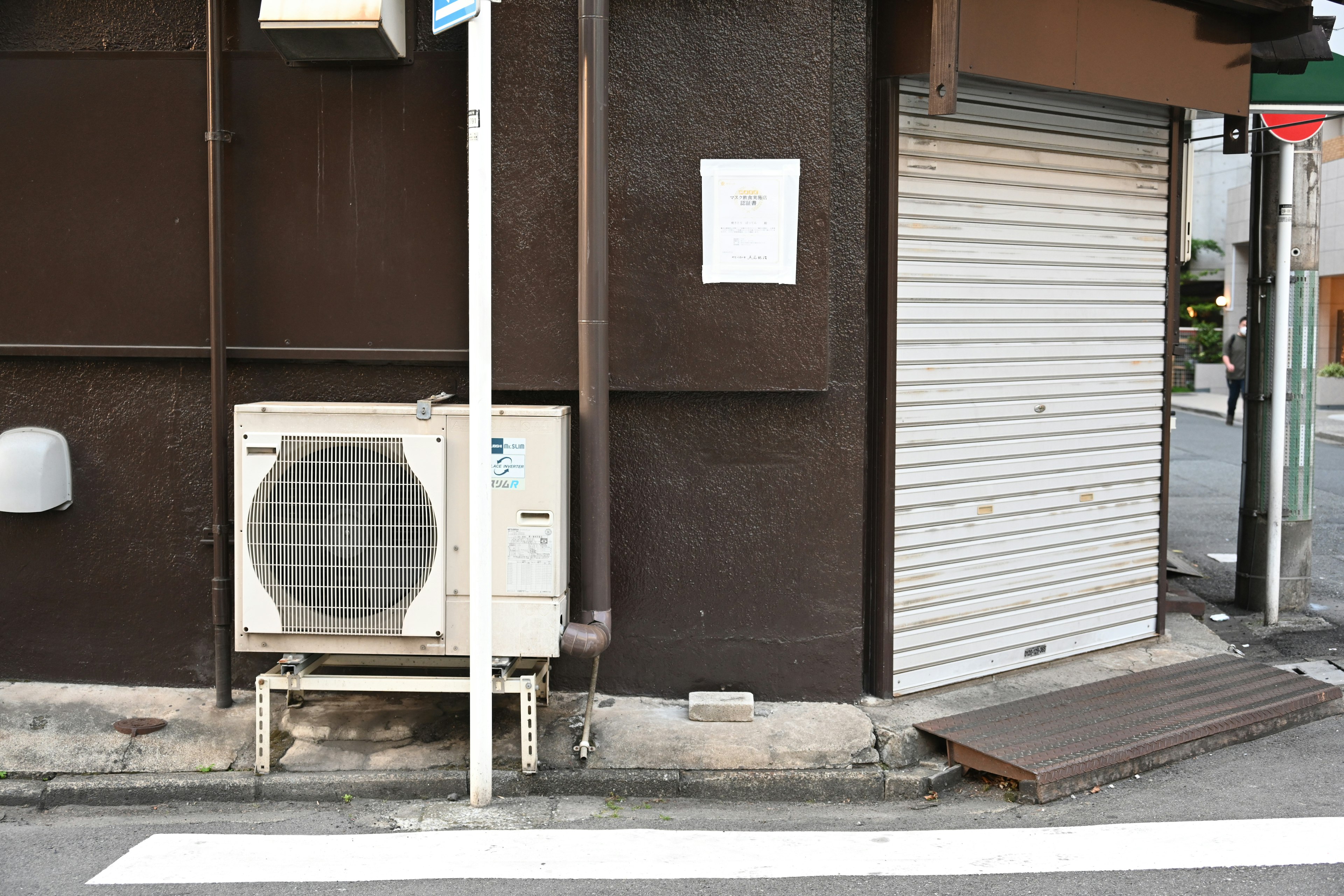 茶色の壁の横に設置されたエアコンとシャッター付きの店舗入り口