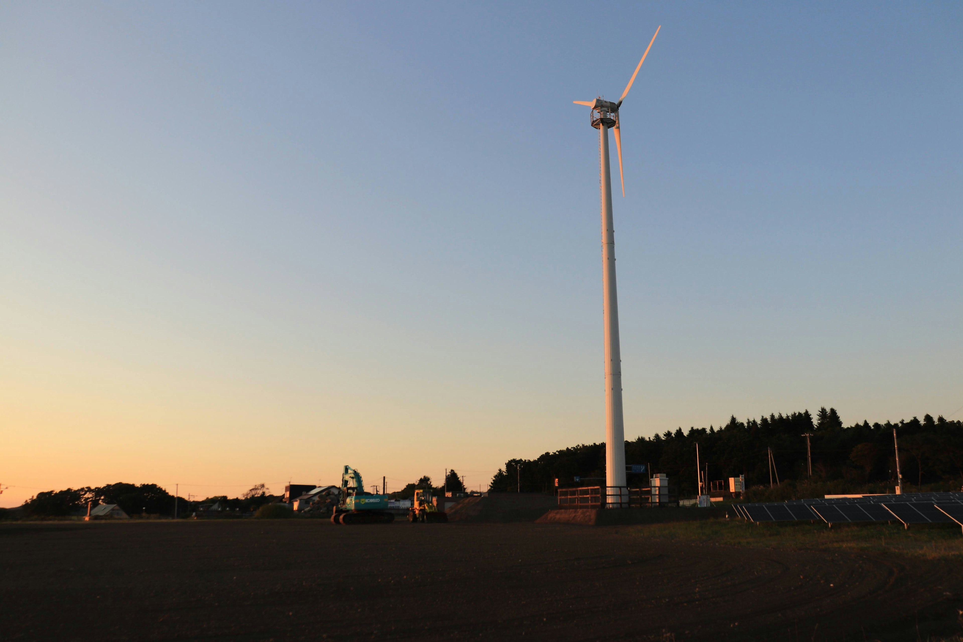 Landschaft mit einer Windkraftanlage vor einem Sonnenuntergangshimmel