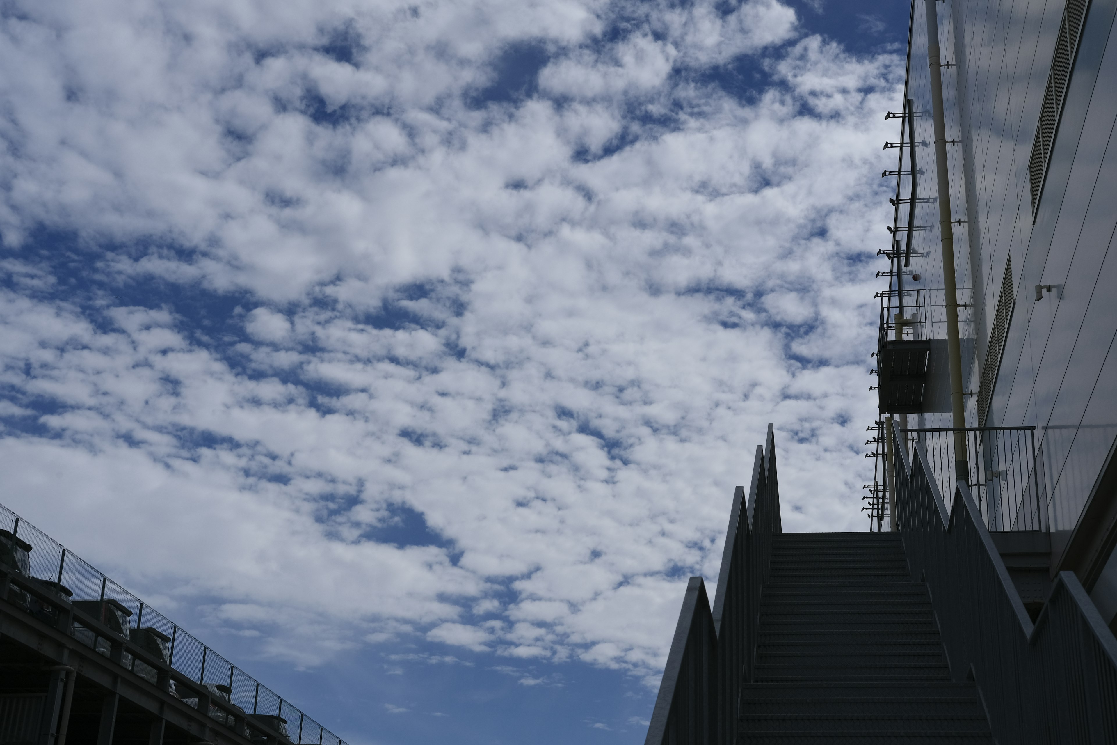 Escalera que conduce a un edificio bajo un cielo azul con nubes esponjosas