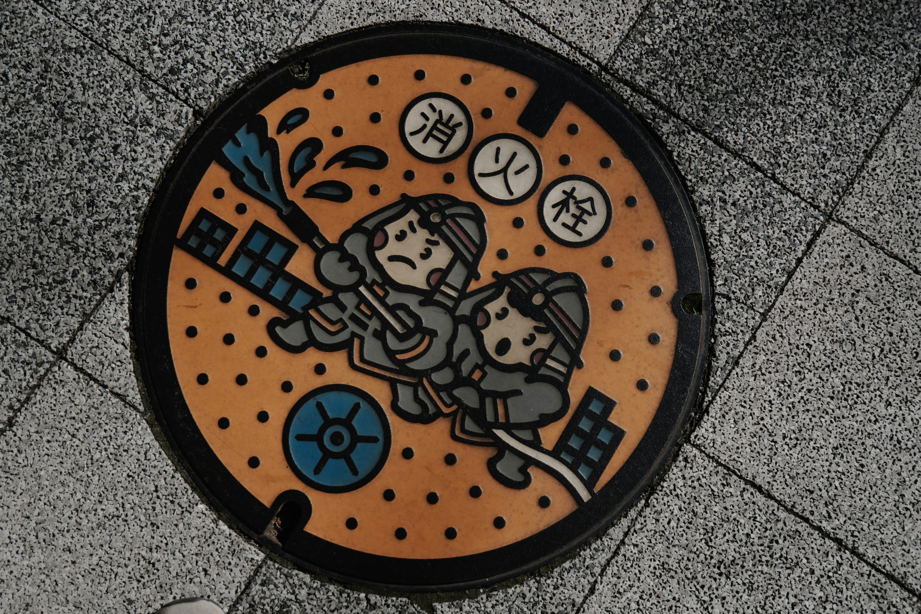 Manhole cover design featuring firefighters spraying water