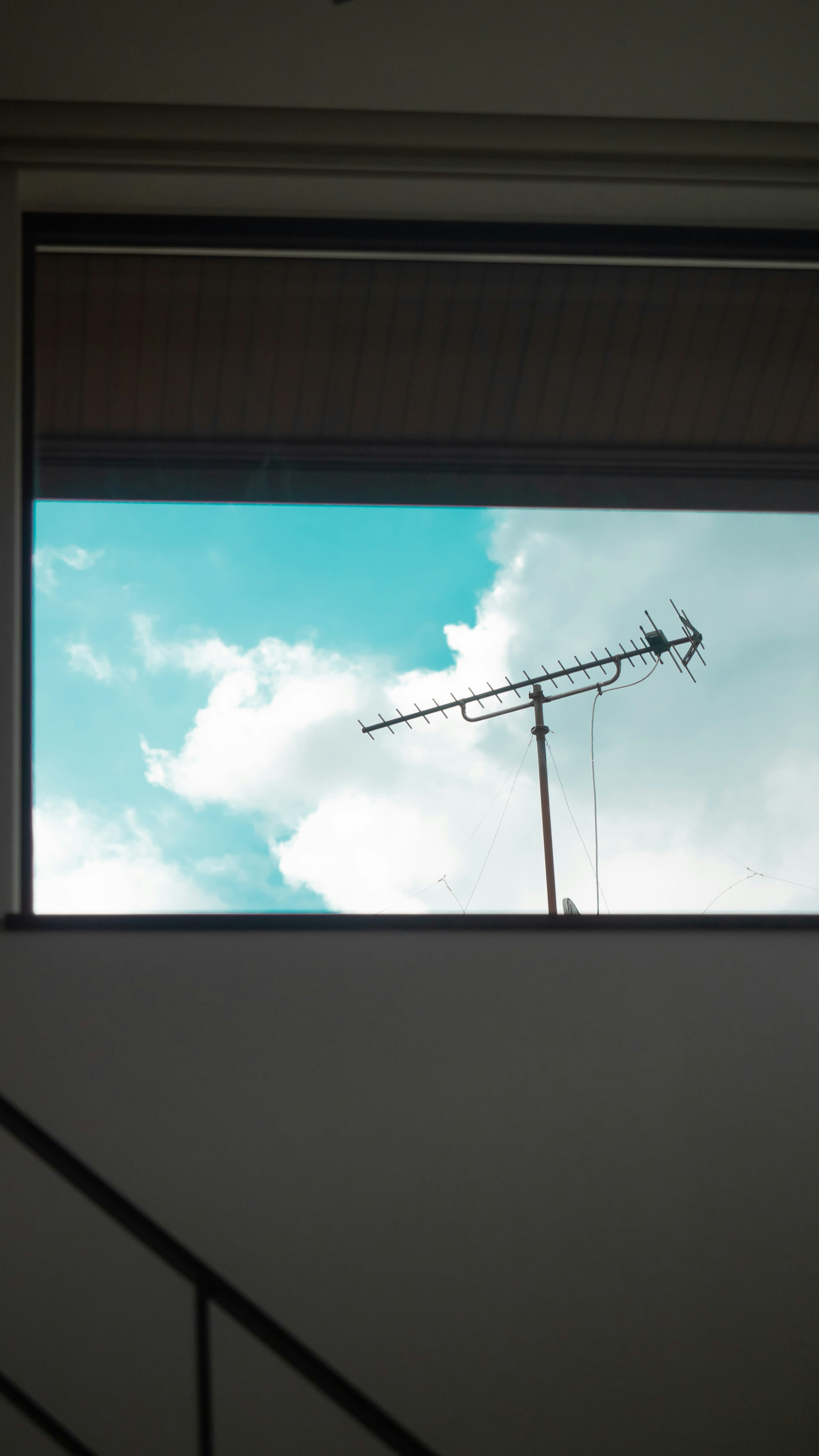 Antenna outside a window with blue sky and white clouds