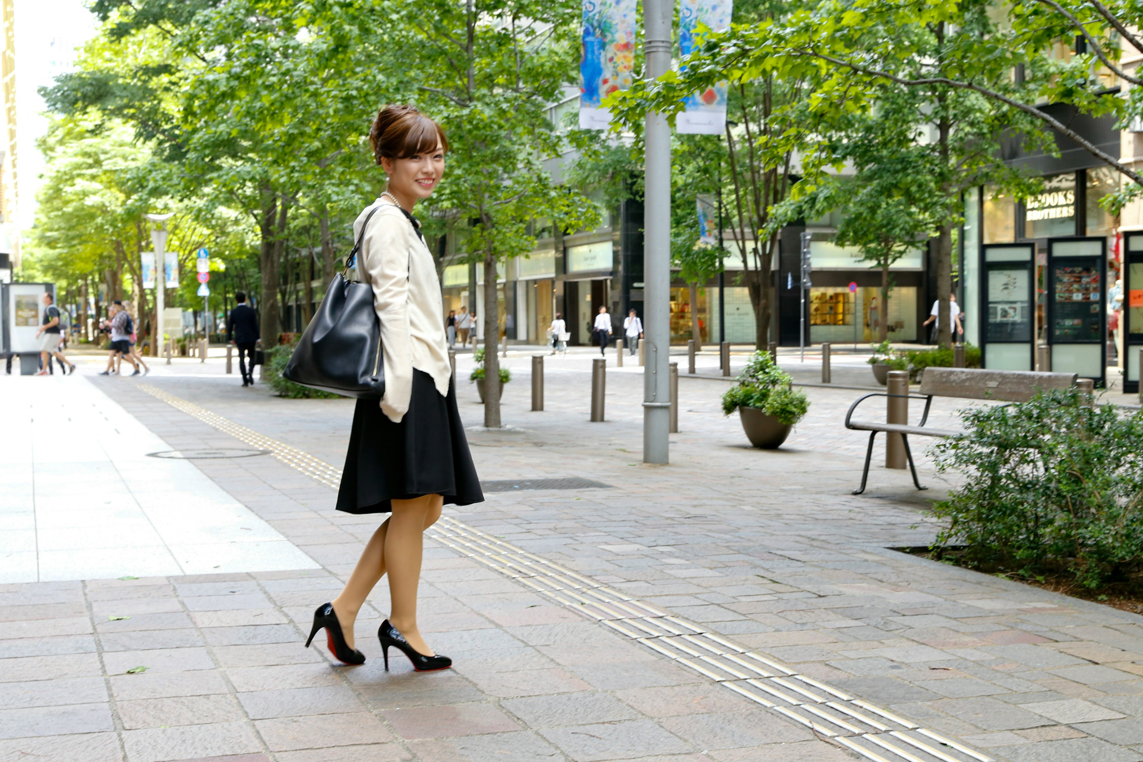 女性が黒いスカートと白いジャケットを着て街を歩いている