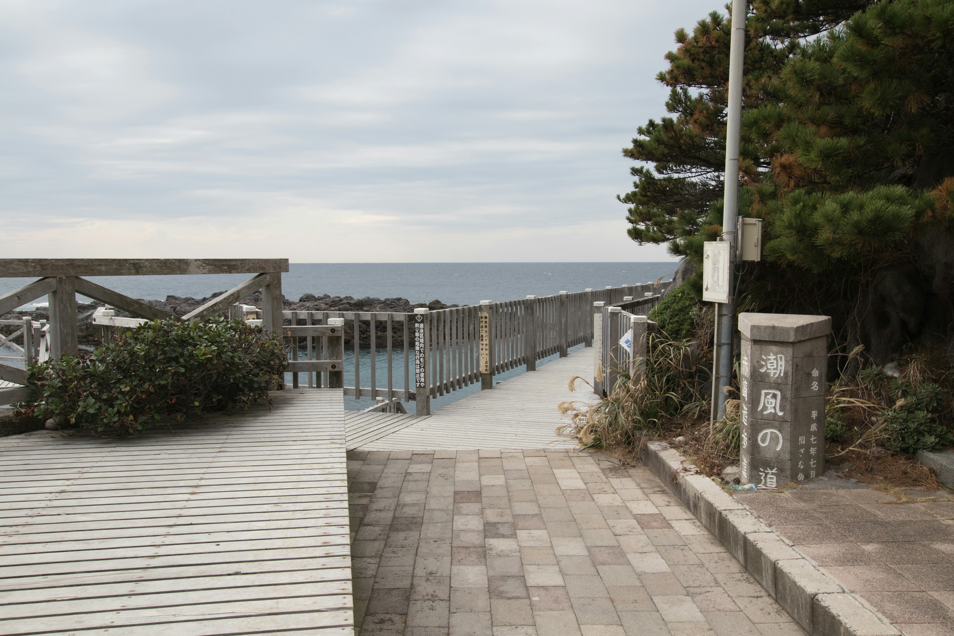 海に面した遊歩道の風景で、木製のデッキとコンクリートの道が見える