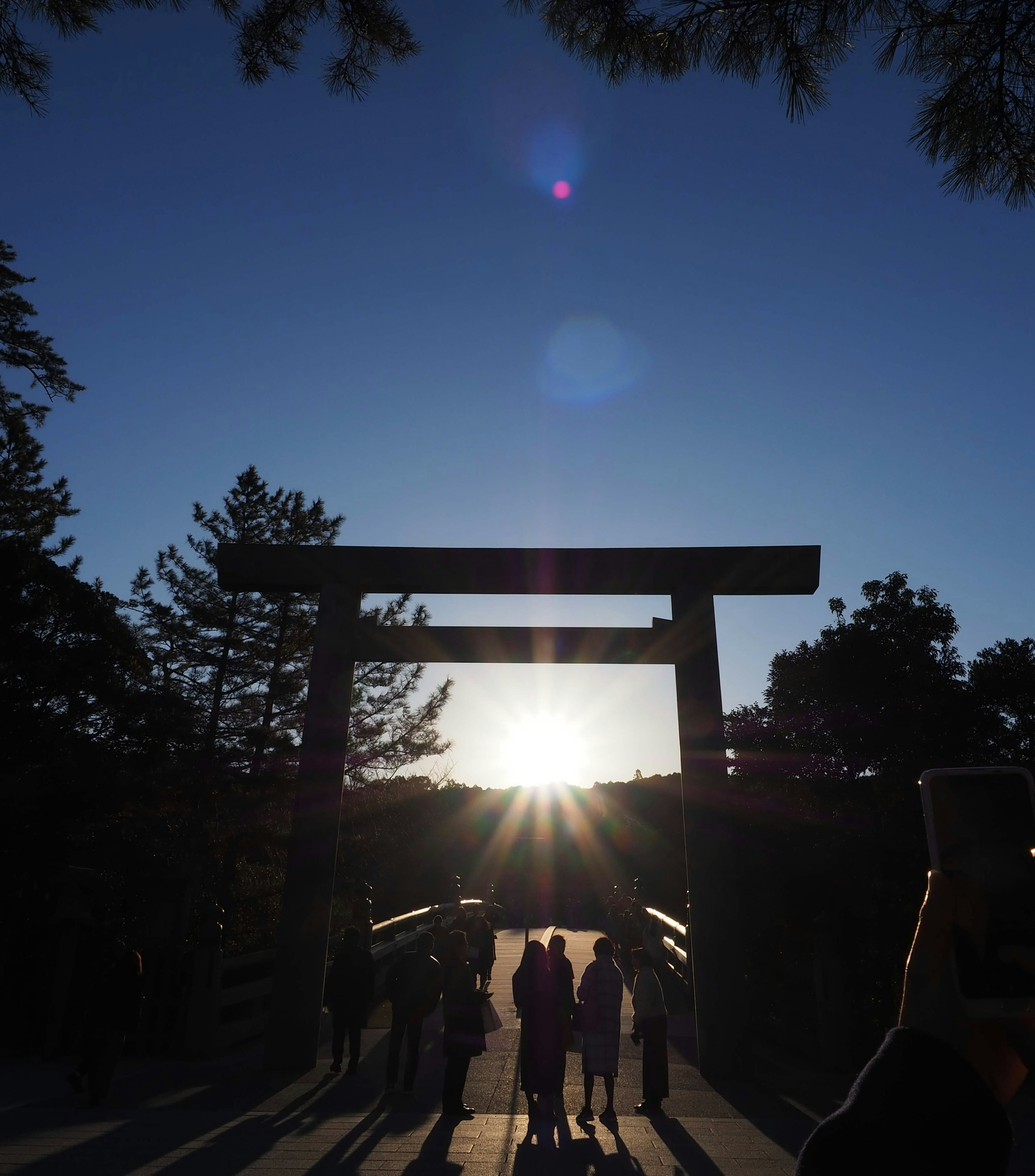 Silhouetten von Personen, die durch ein Torii mit Sonnenuntergang im Hintergrund gehen