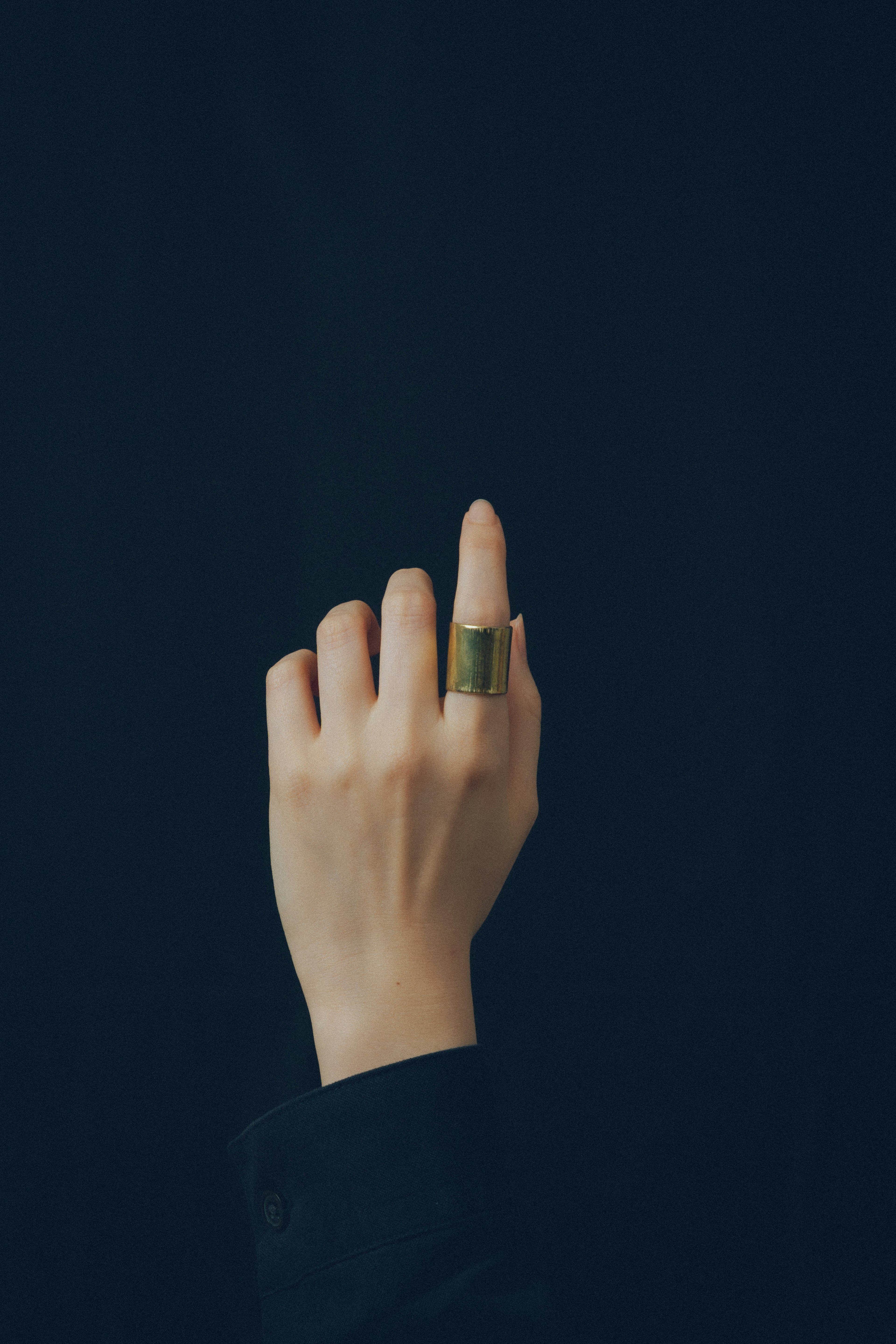 Hand with a green ring pointing upward against a dark background