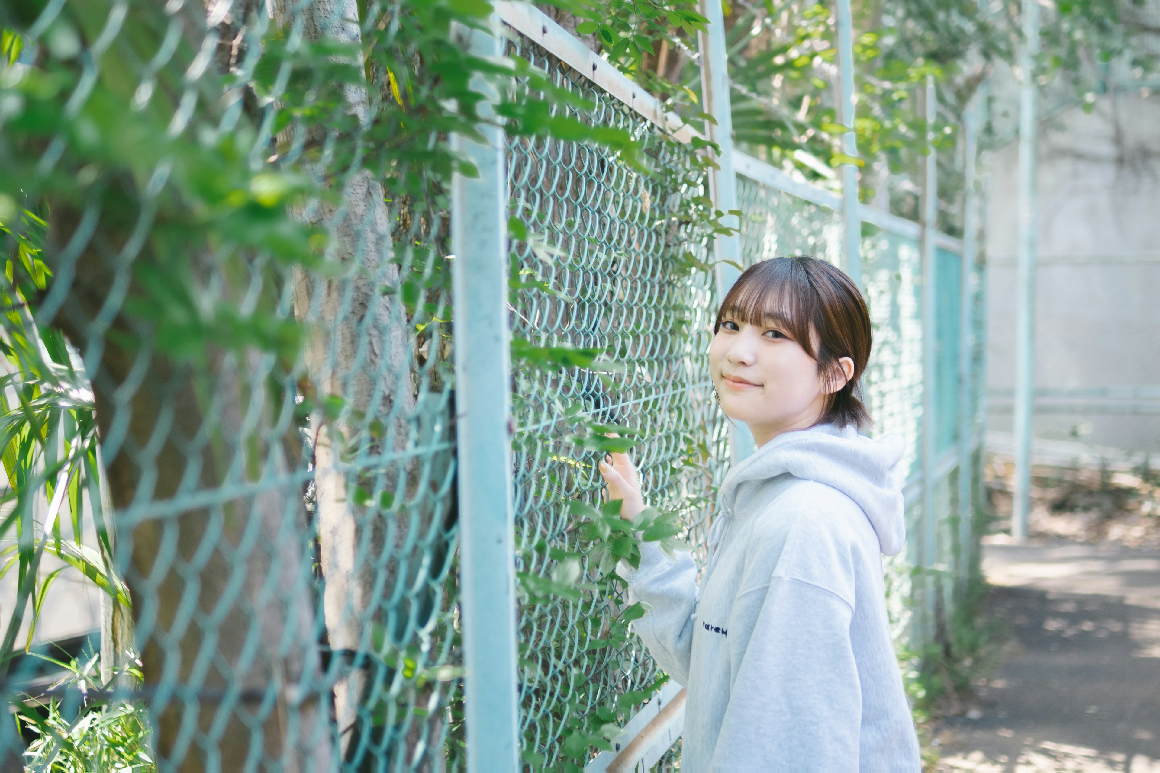 Mujer sonriendo junto a una cerca verde con vegetación