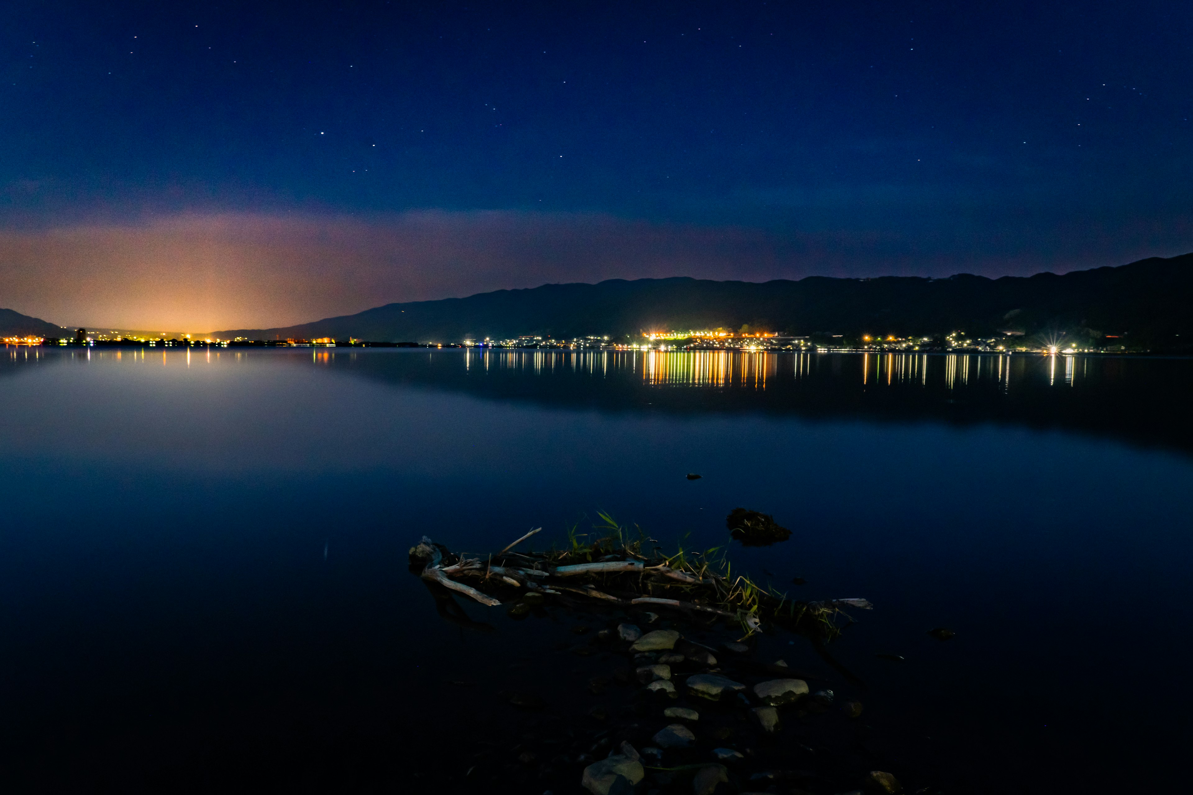 夜空に星が輝く湖の風景 水面に映る街の明かりと山々