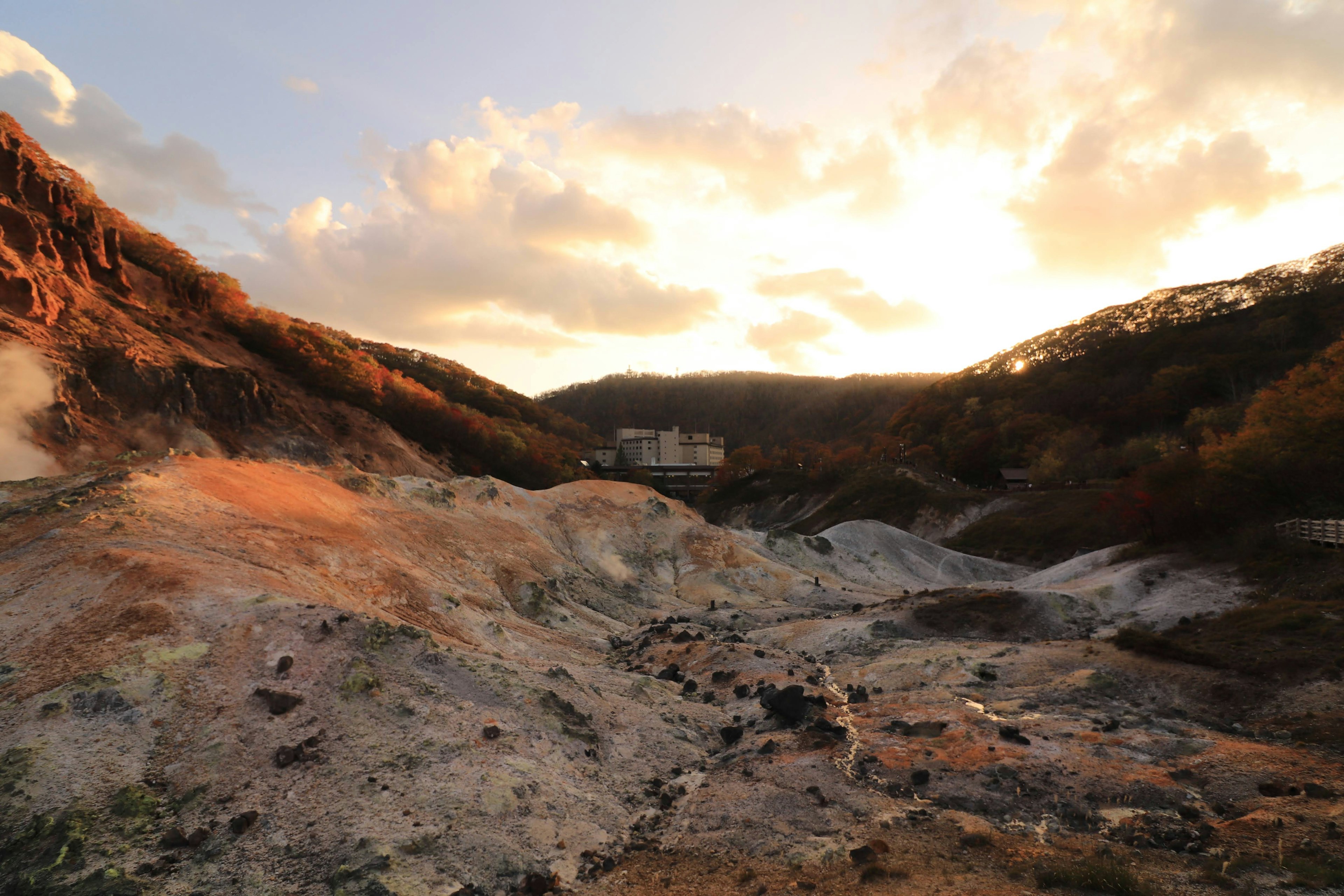 夕焼けに照らされた温泉地の風景 雄大な山々と広がる硫黄の地面