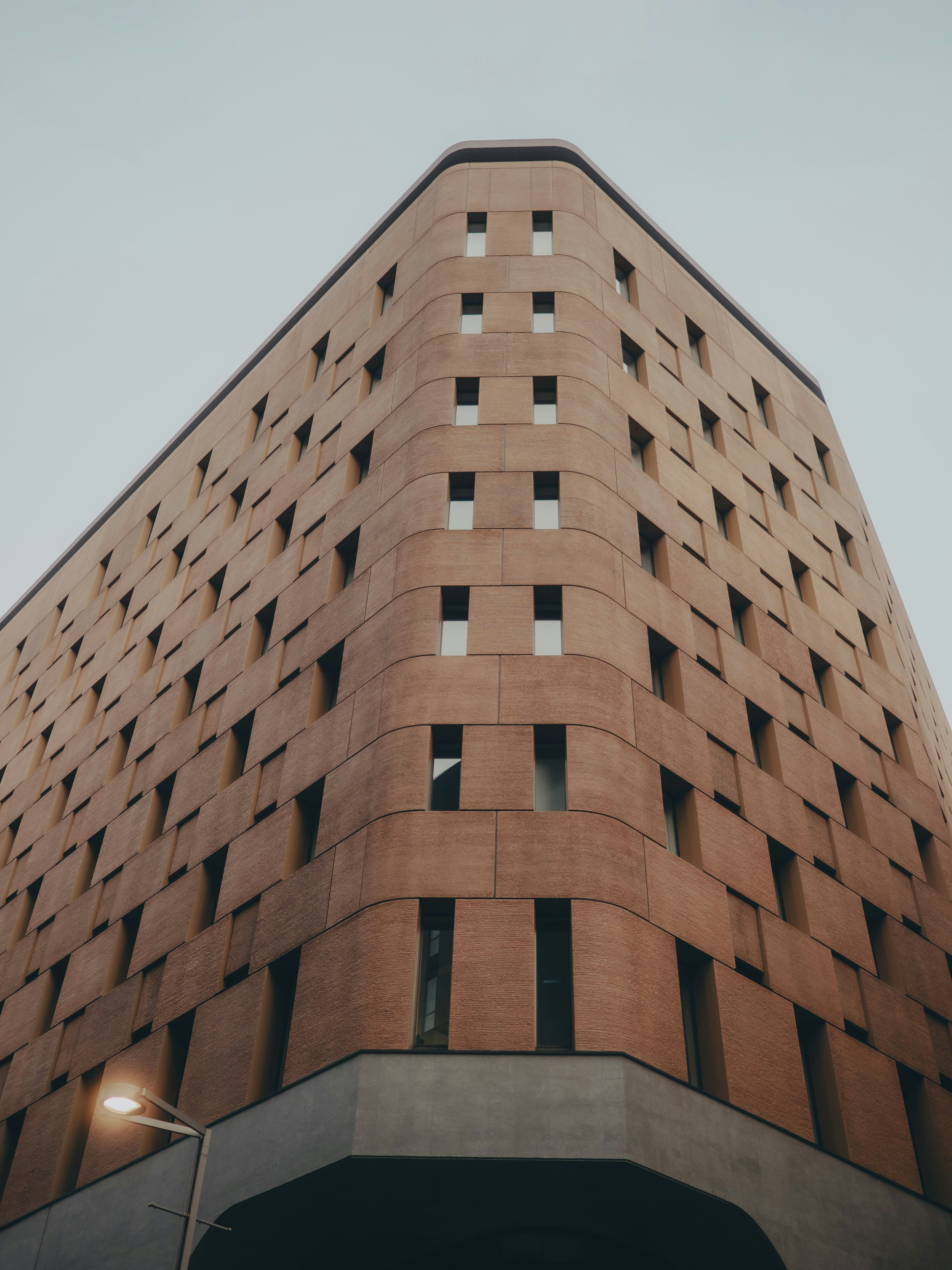 角度のある現代的な建物の外観 照明がある街灯と曇り空