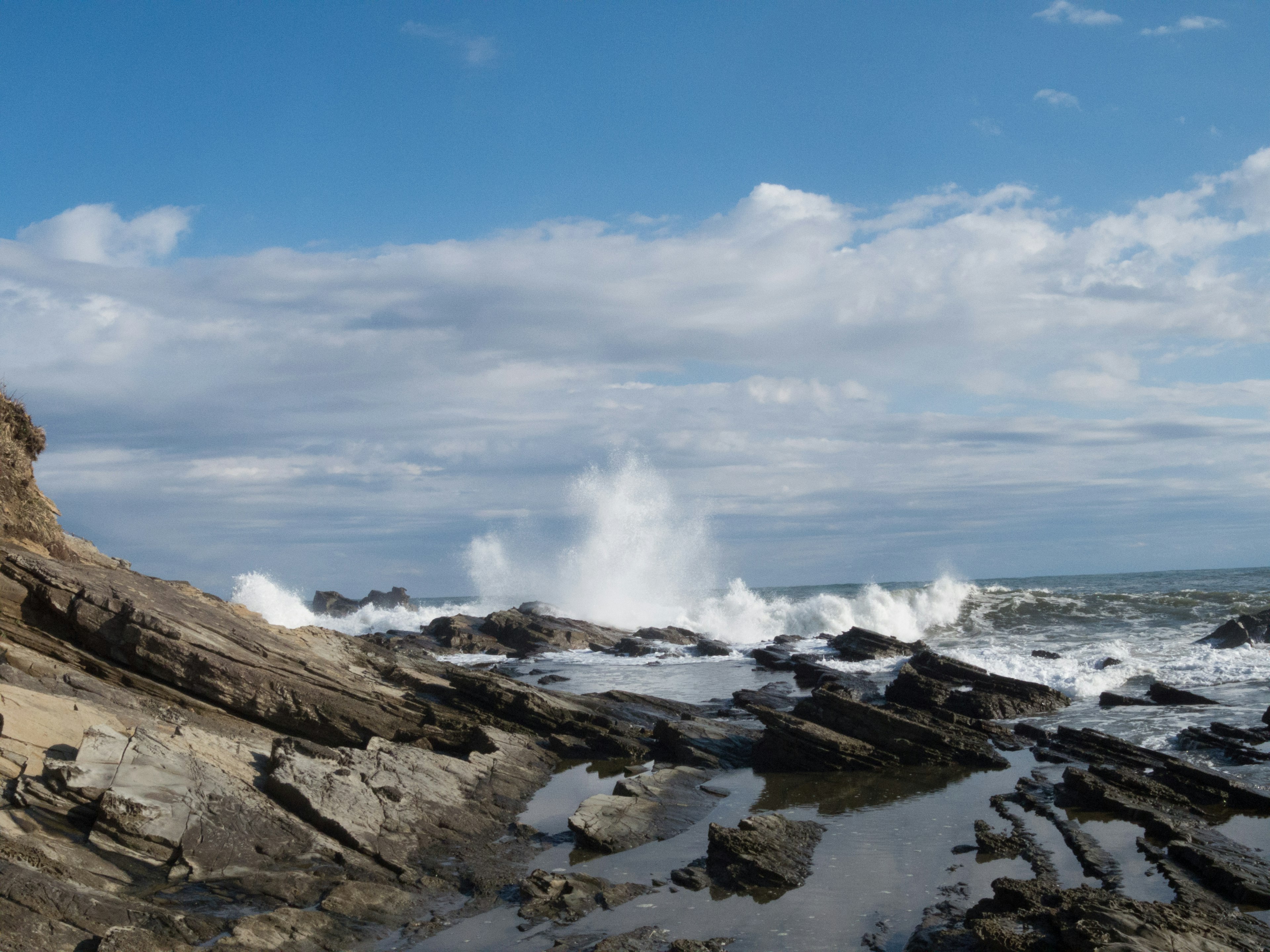 Pemandangan pantai dengan ombak menghantam batu