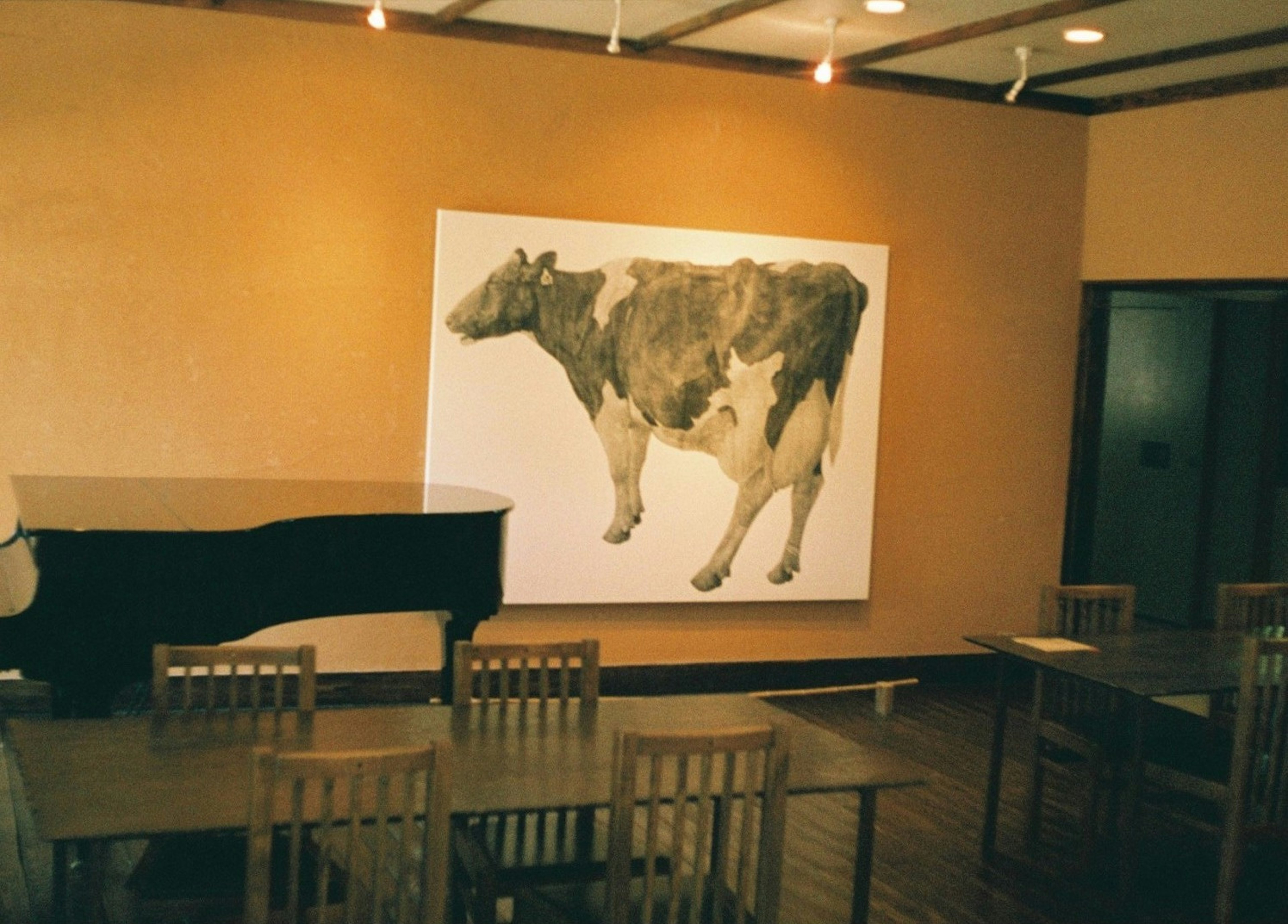 Interno di un caffè con un grande dipinto di una mucca sulla parete e un pianoforte