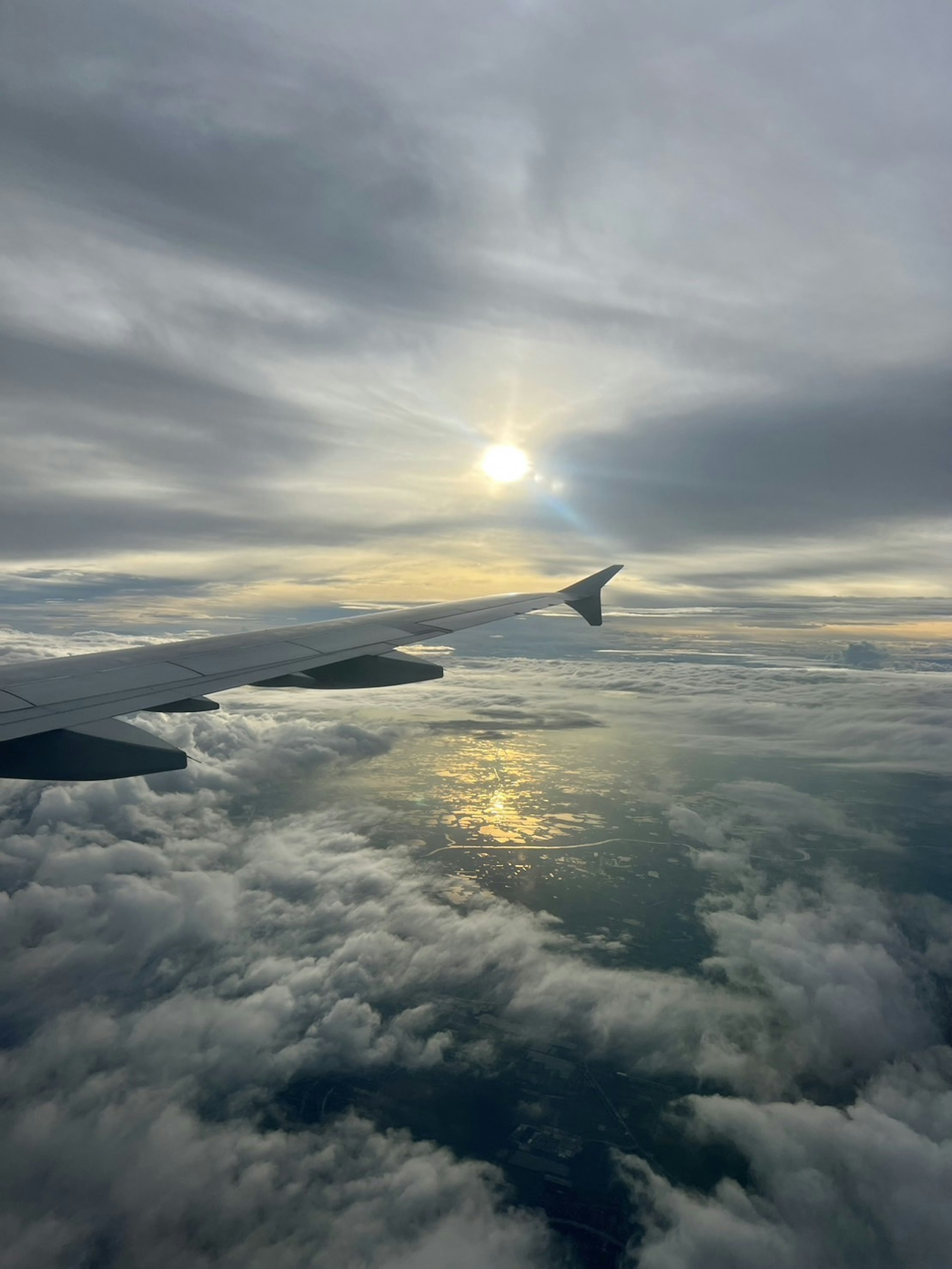 Vista de un ala de avión sobre las nubes con un atardecer reflejándose en el agua