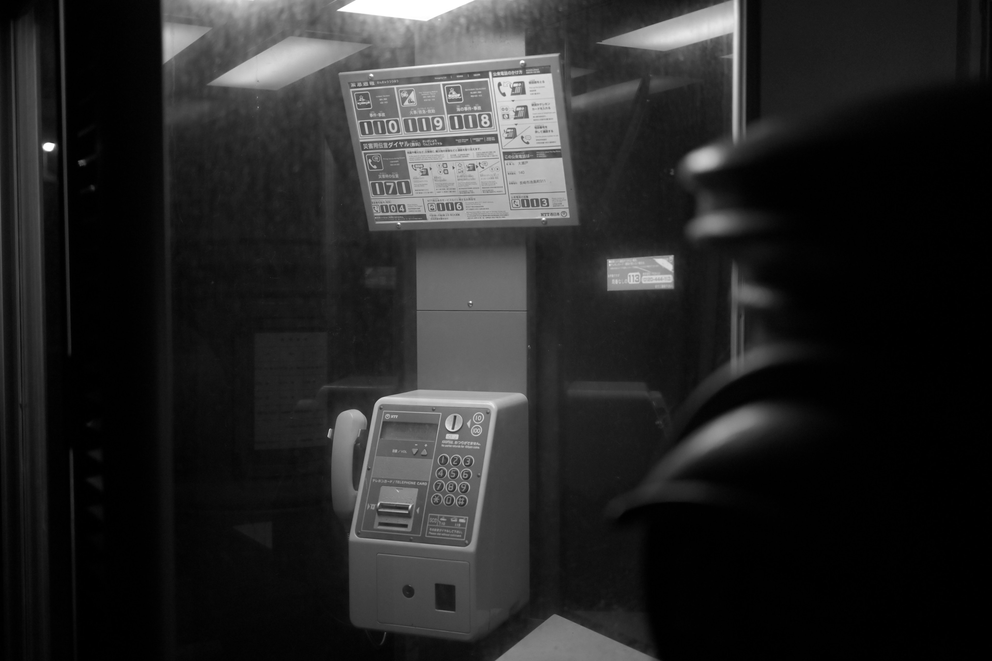 A public telephone inside a phone booth with a display panel visible