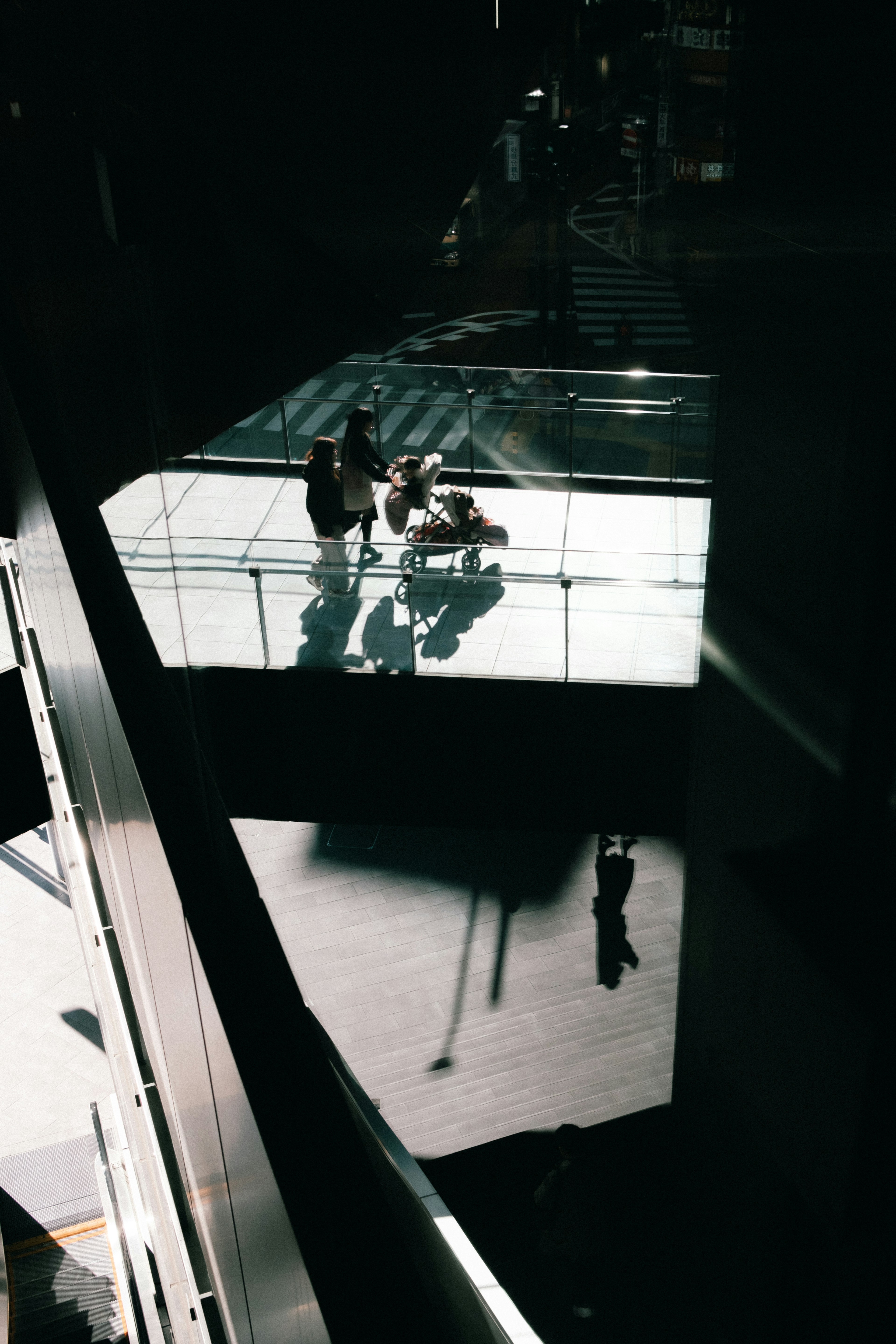 Silhouettes of people on a glass bridge illuminated against a dark background