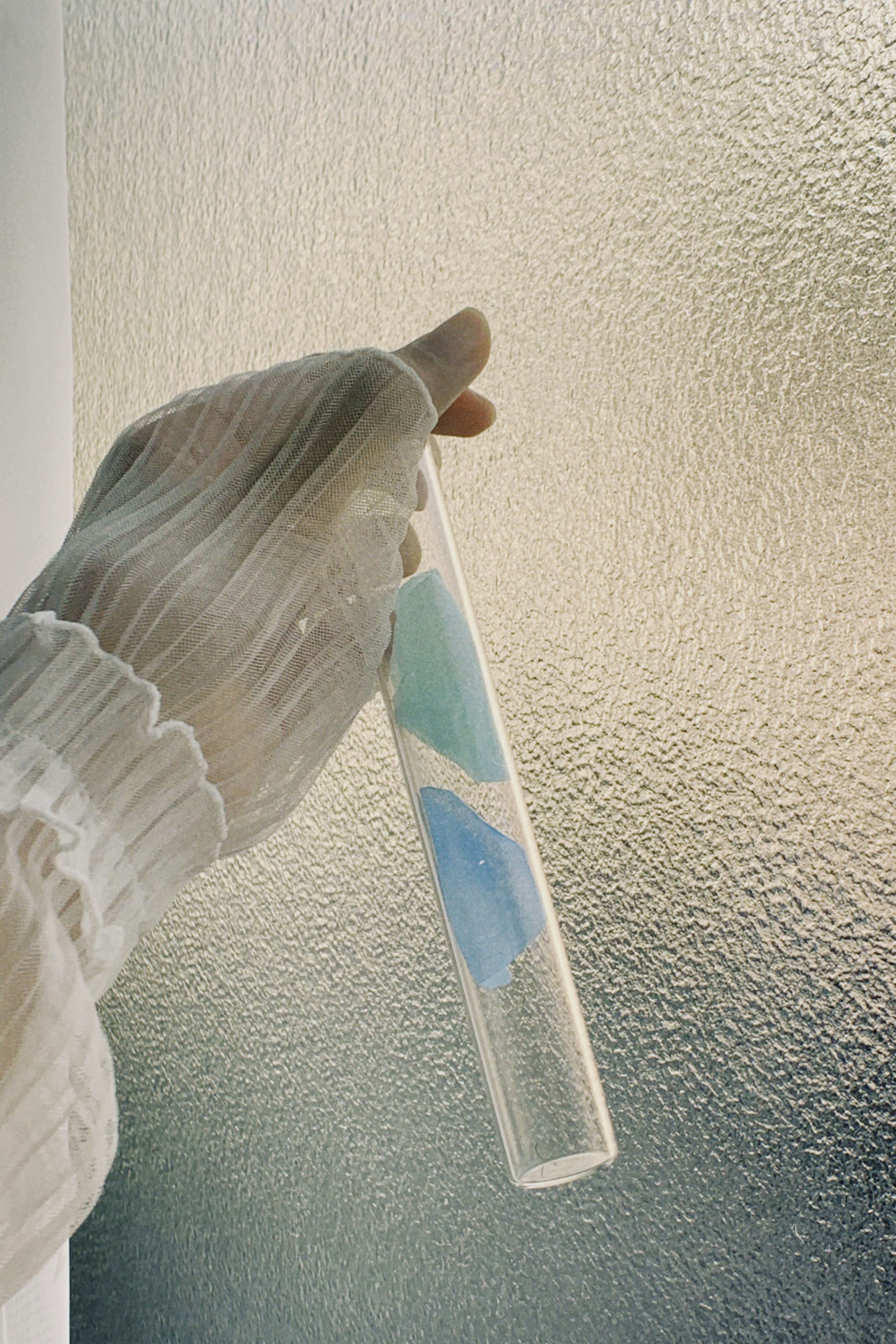 A gloved hand holding a transparent test tube with blue liquid inside