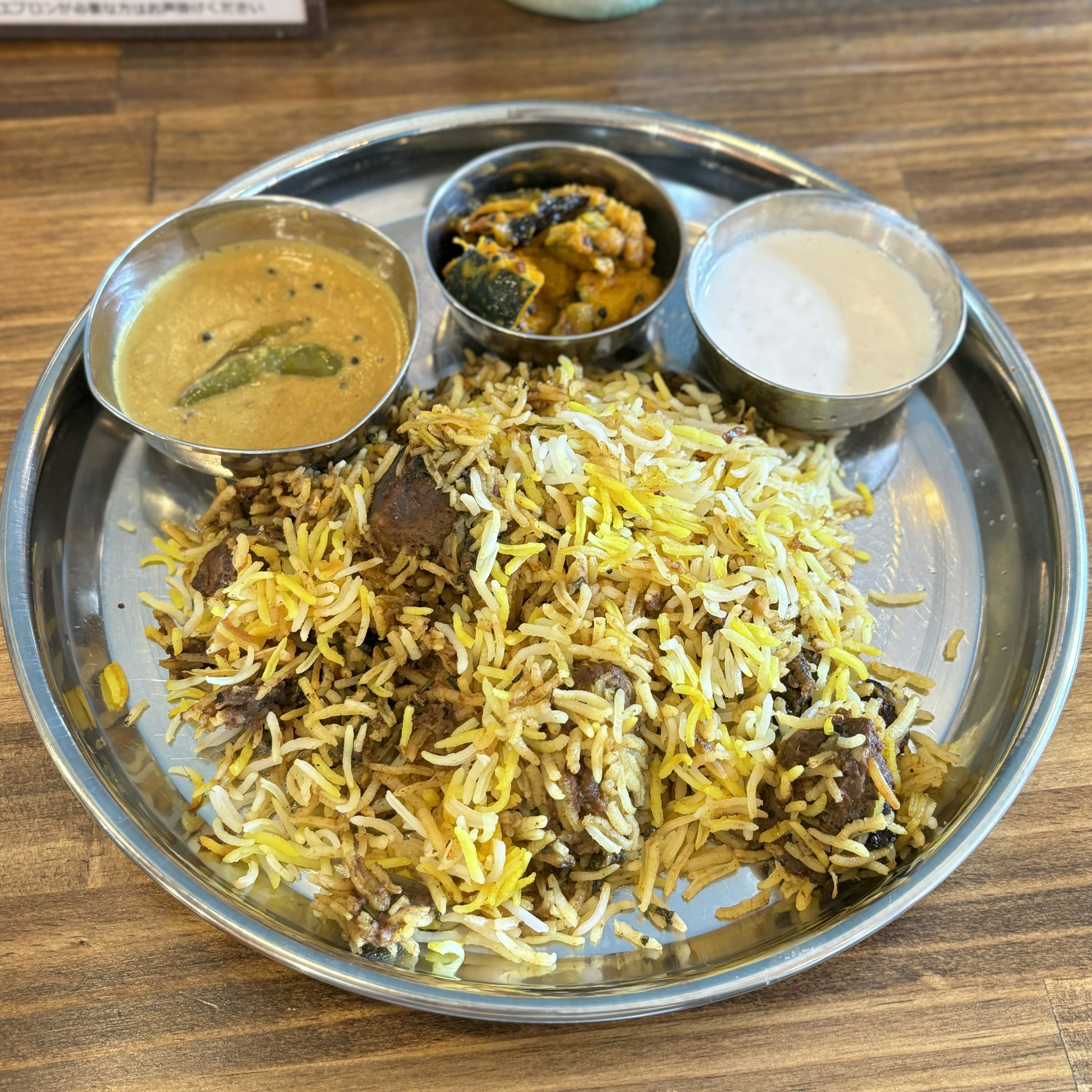 A metal plate featuring aromatic biryani with side dishes including curry and raita